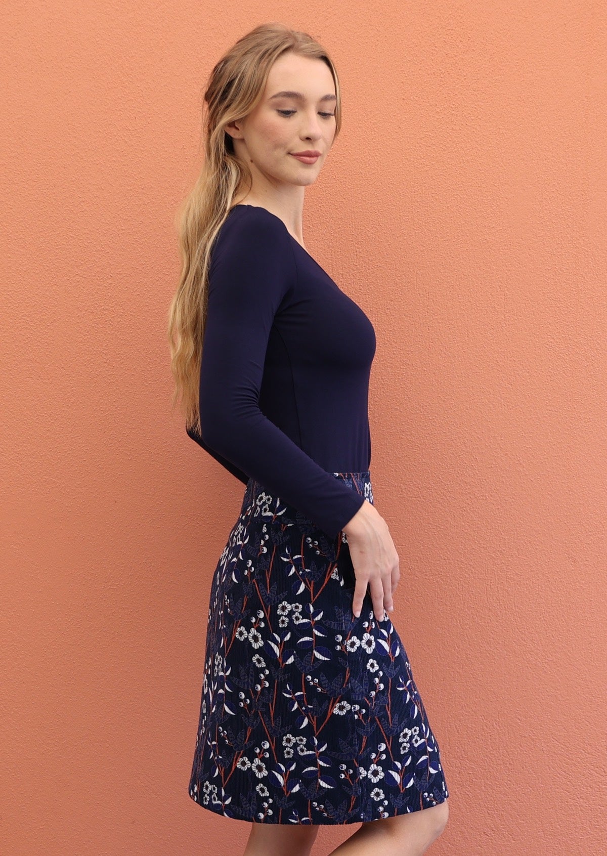Model poses sideways wearing a beautiful floral printed above knee length skirt paired with long sleeve top navy blue .