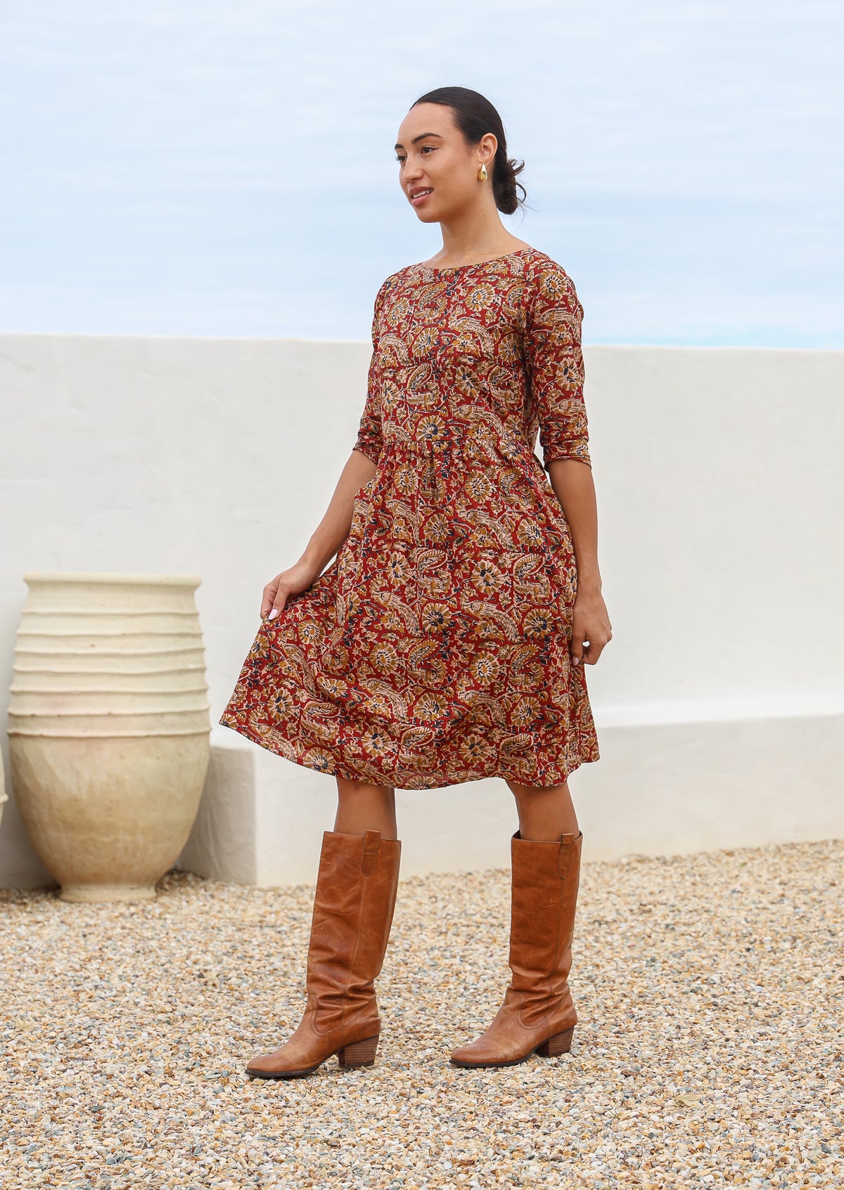 Model standing slightly sideways wears 100% cotton, midi length dress in earthy floral tones.