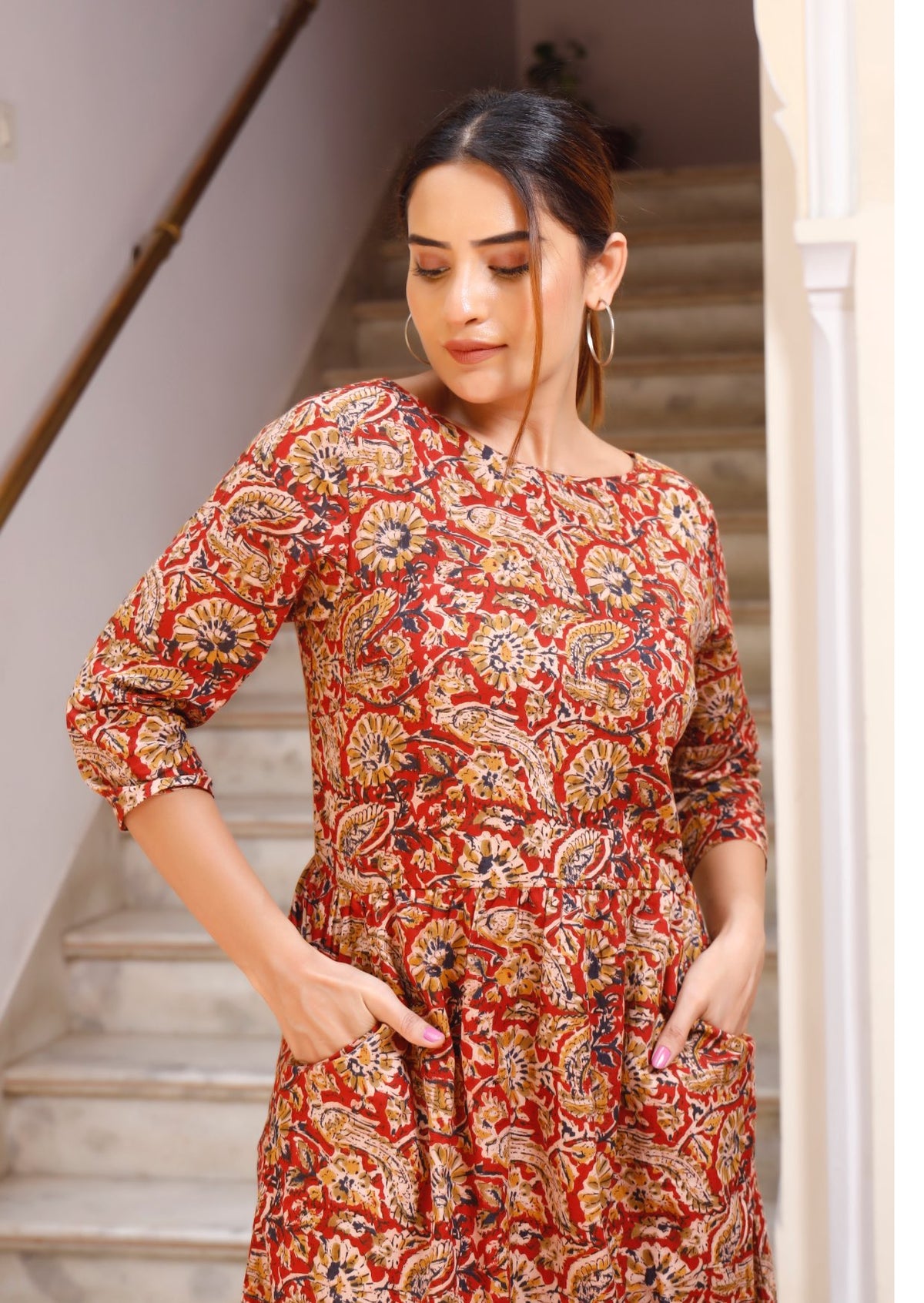Close up image of model in 3/4 sleeved, floral print cotton dress with round neckline, pockets and small pin tucks at the waist.
