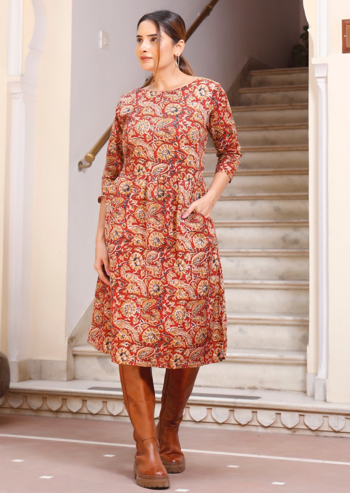 Model standing in front of stairs wears relaxed fit dress with simple round neckline and pocket.