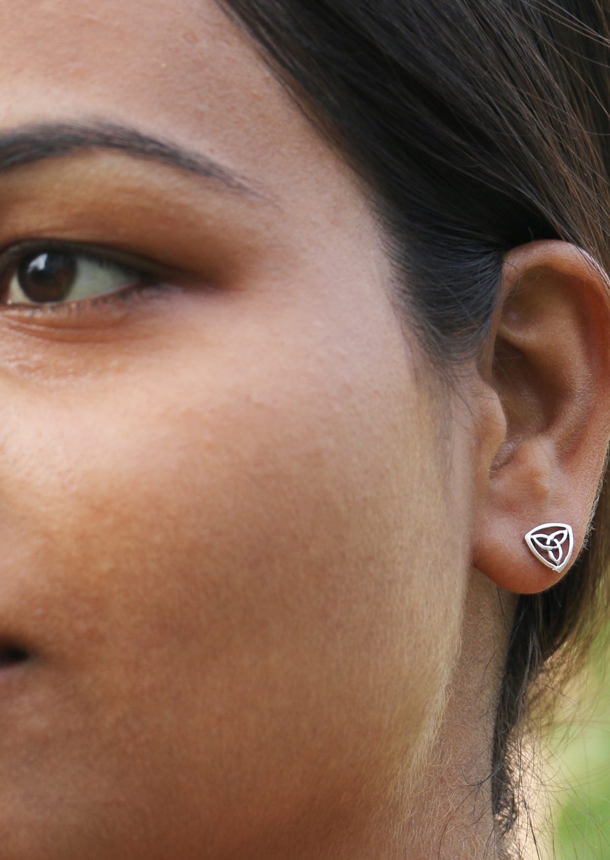 Close-up of a person wearing a silver celtic triangle stud with intricate trinity knot design