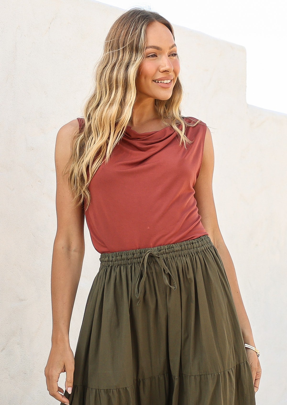 Woman wearing a deep terracotta coloured sleeveless top and olive green skirt against a white background