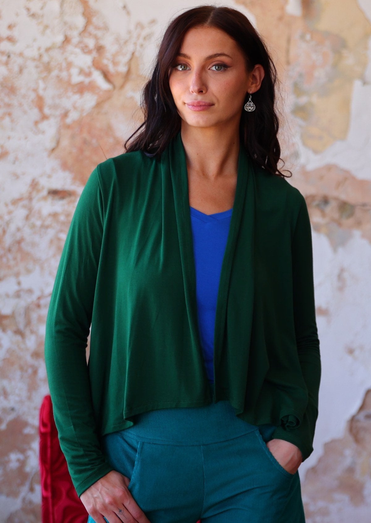 Woman wears forest green long sleeve stretch rayon cardi with a waterfall front hem that is cropped at the front