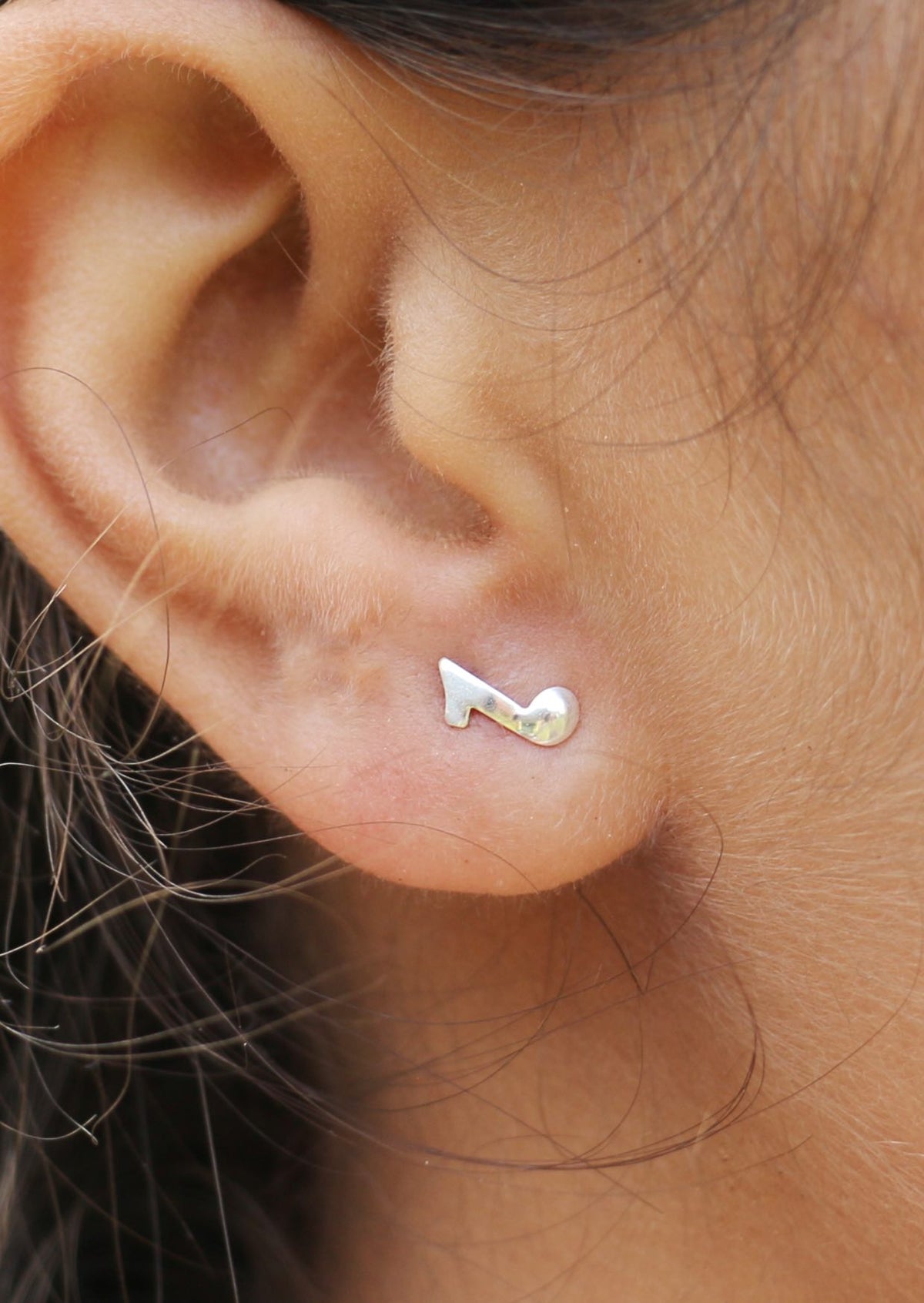 Sterling silver eight note quaver studs displayed on a woman's ear with butterfly backs