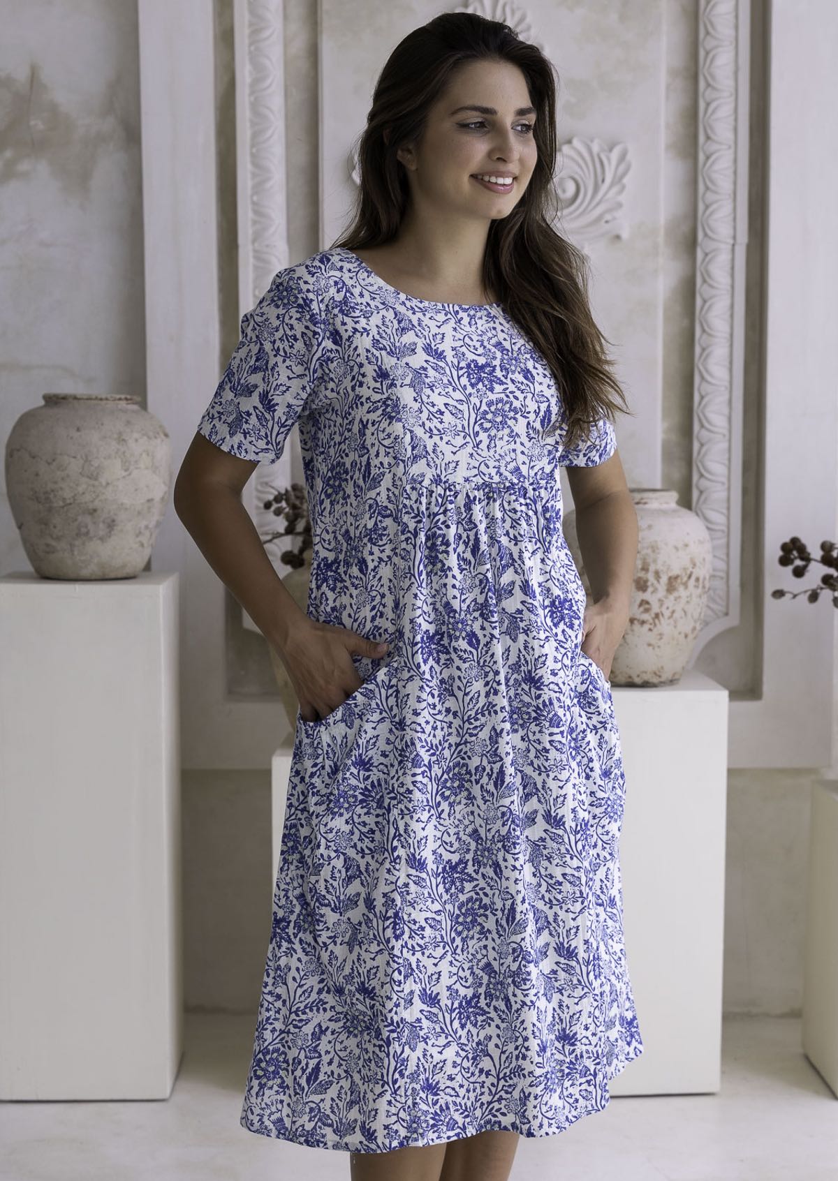 Woman wearing a blue floral cotton dress standing in a neutral setting.