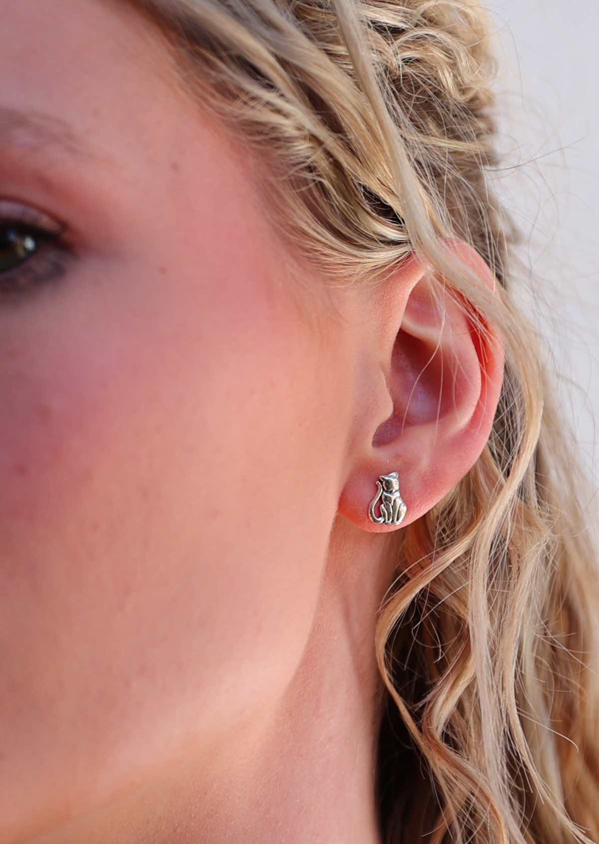 Close-up image of a person wearing Happy Cat silver cat-shaped stud earrings.