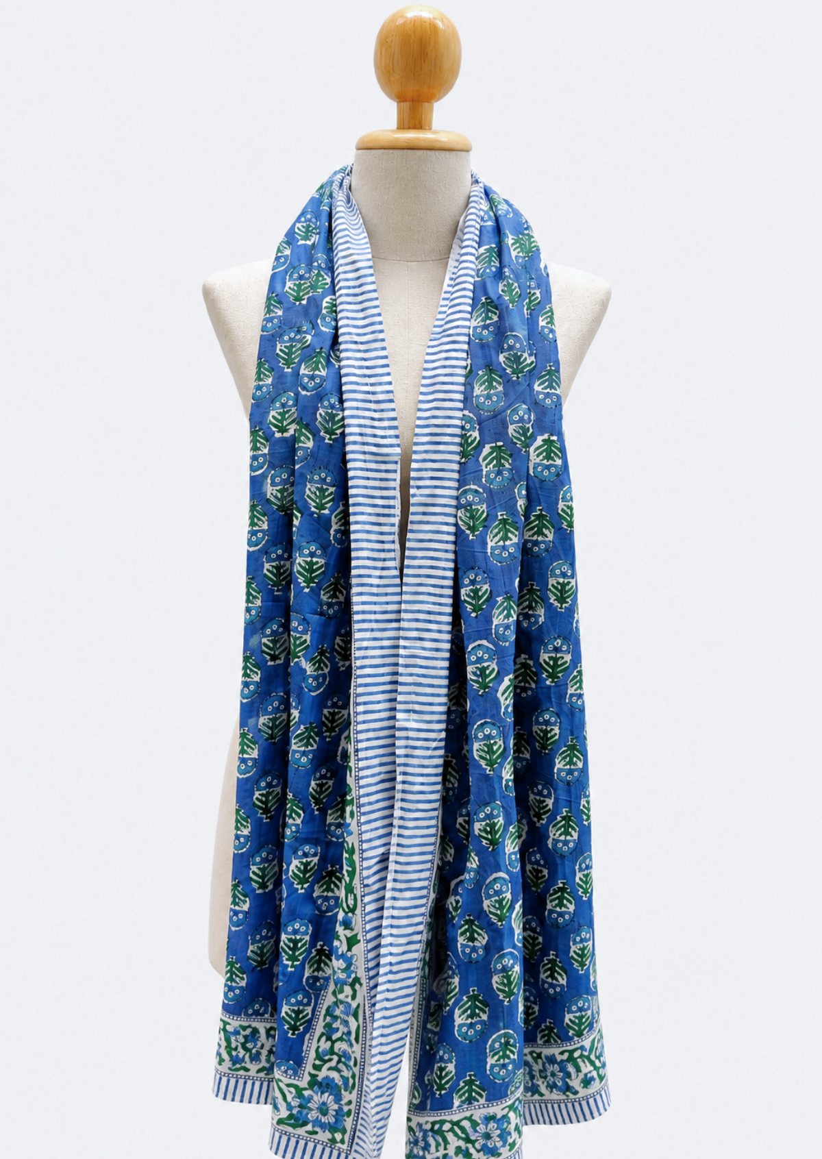 A blue scarf with green floral block prints and a blue-and-white striped center panel, draped on a cream dress form against a light gray background.