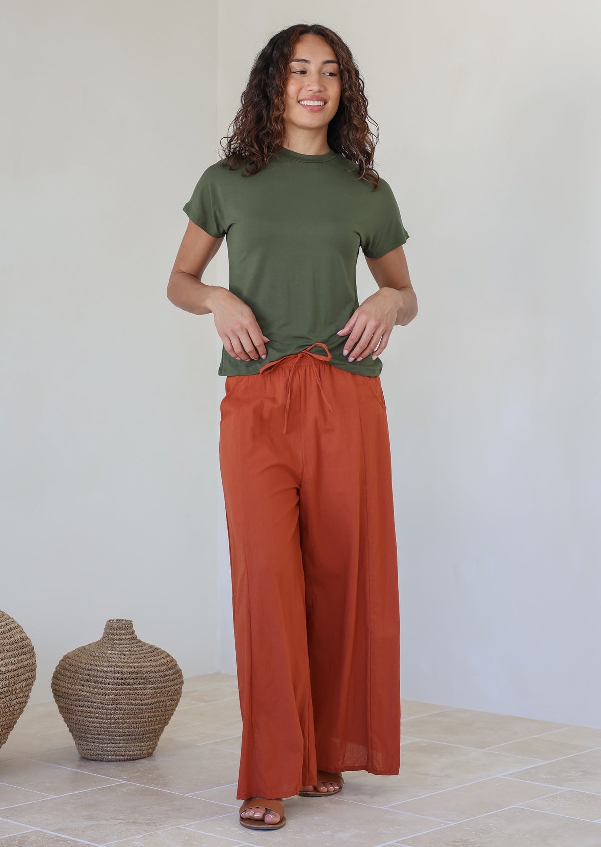 Woman wearing an olive green t-shirt and rust colored wide-leg pants with drawstring tie and pockets
