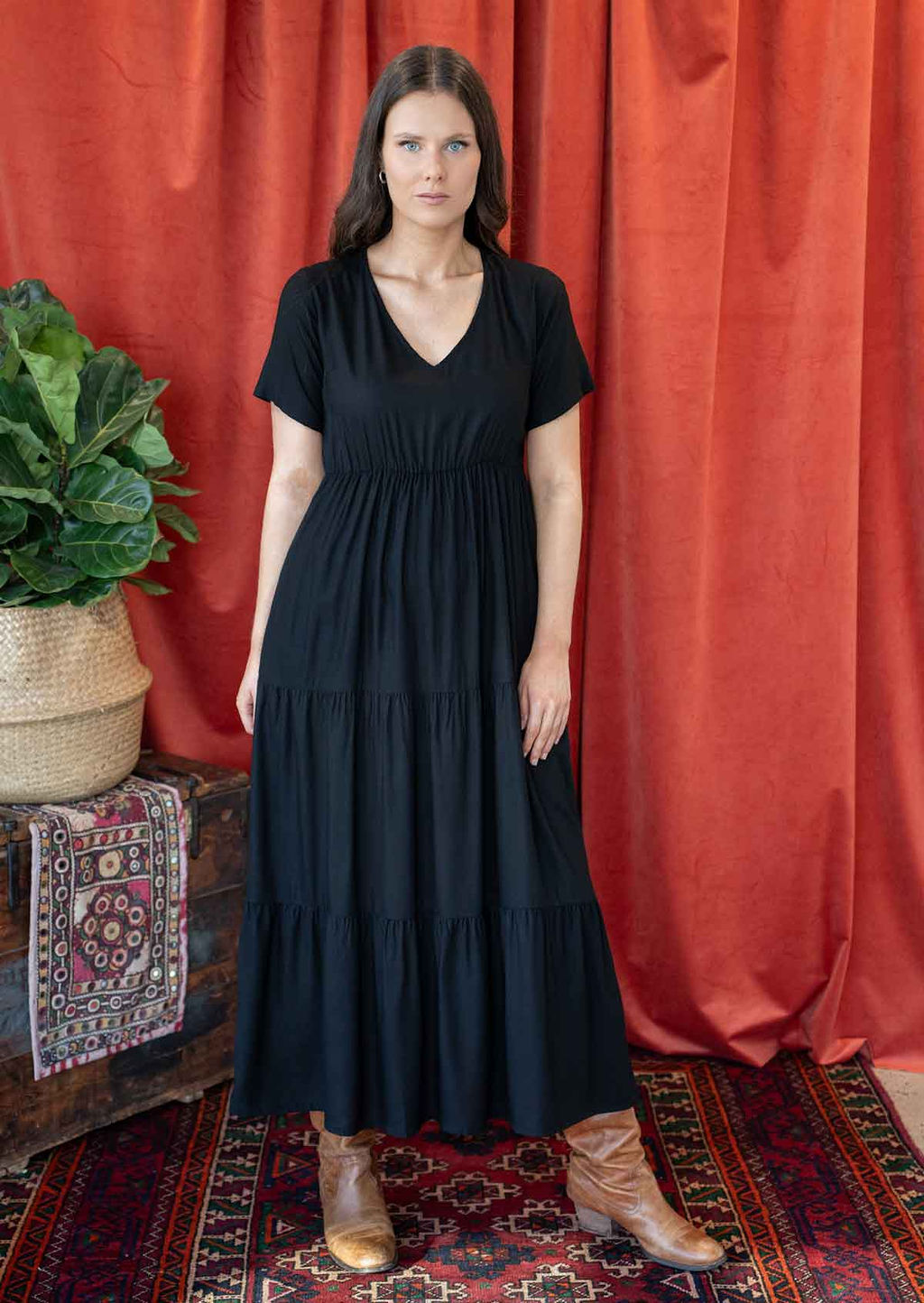 Woman wearing a black maxi dress standing in front of a salmon coloured curtain