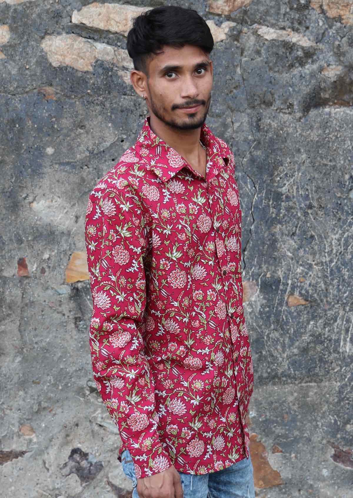 Man wears long sleeve cotton button through shirt with collar and coconut buttons, in cranberry based floral print