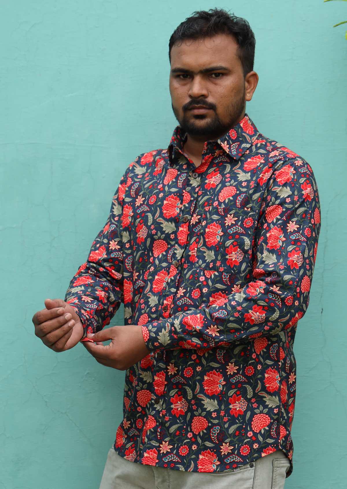 Man wearing a colourful floral long sleeve collared shirt against an aqua background