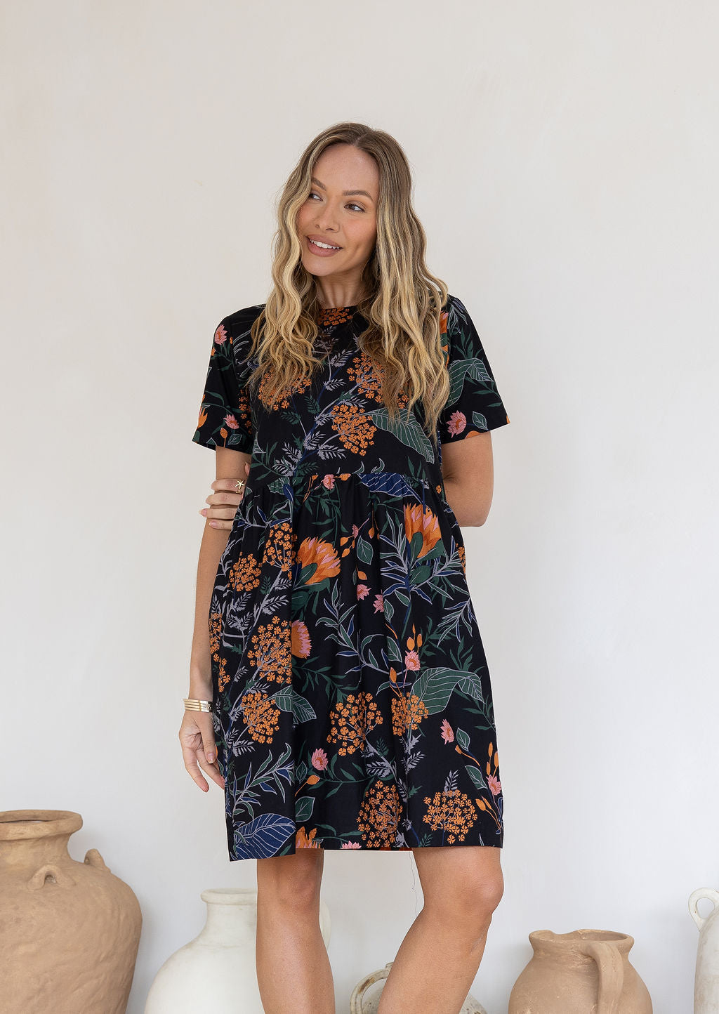 Woman standing in front of white wall wears above knee length, loose fit retro dress in gorgeous botanical print.