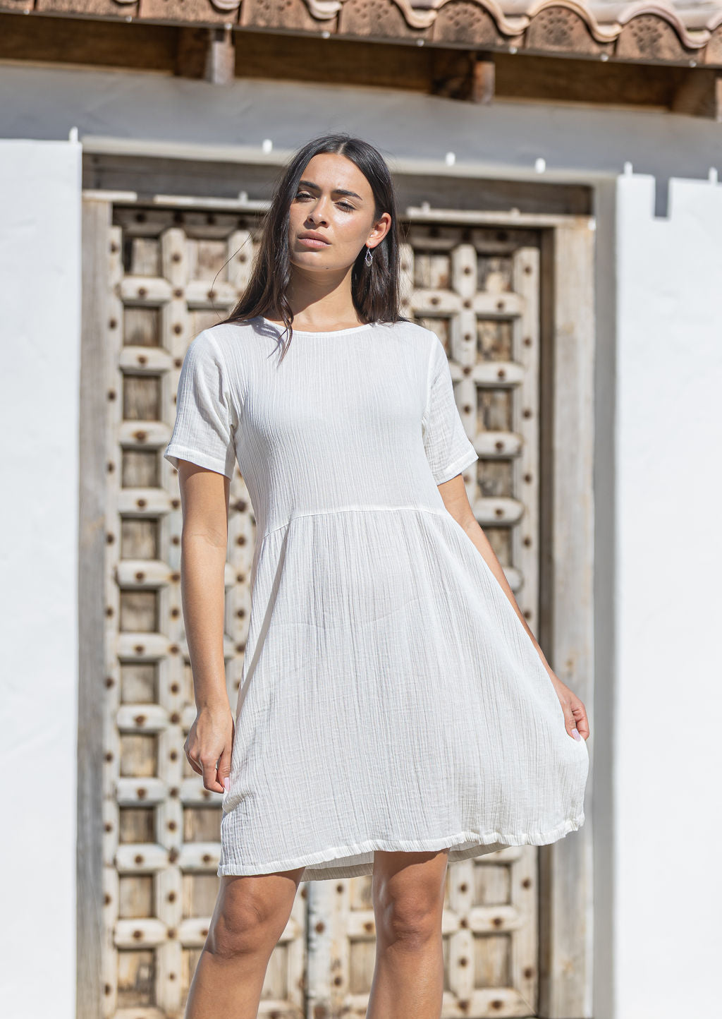 Woman wearing a white cotton sundress standing in front of a textured wall.