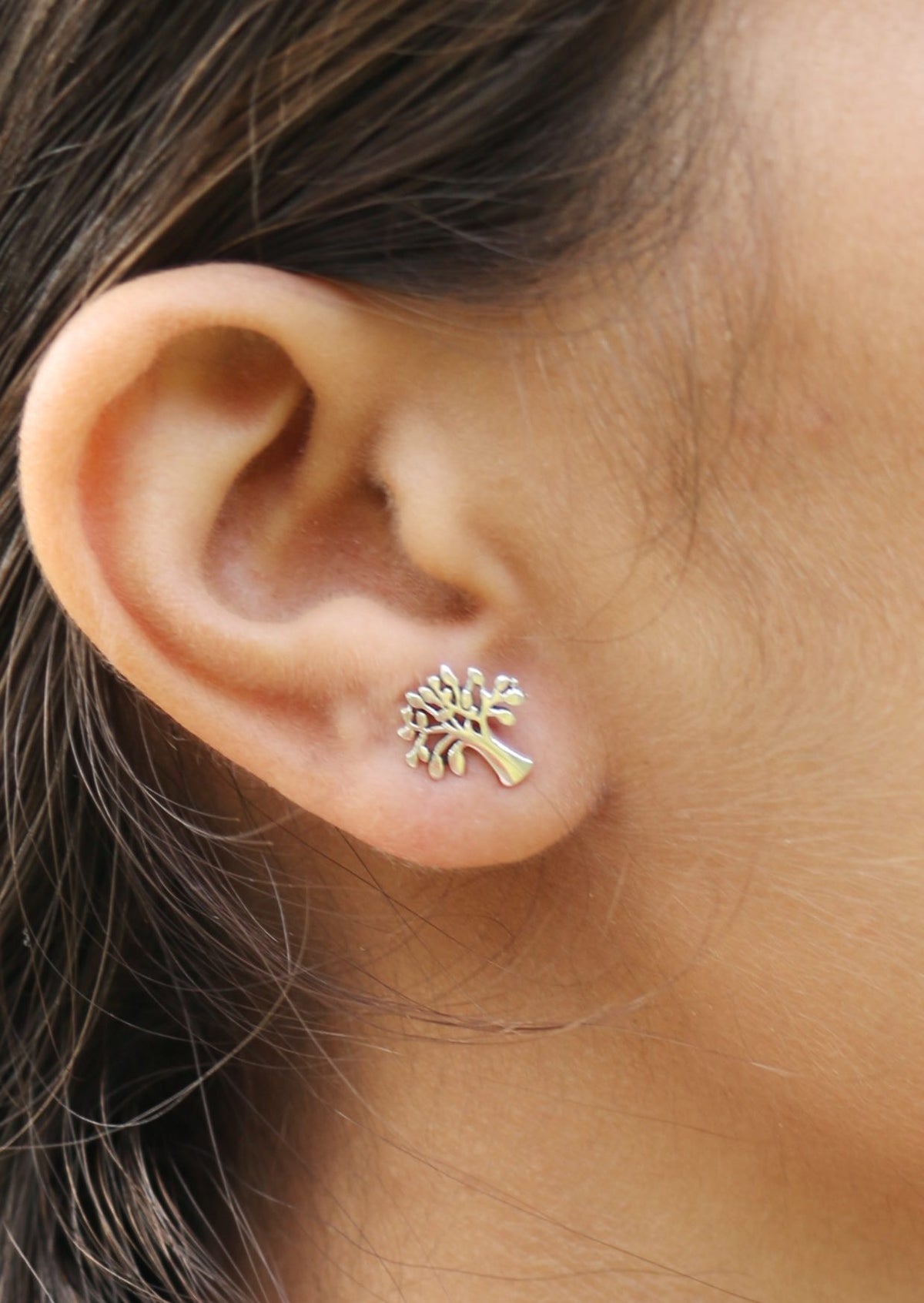 Person wearing a mango tree shaped sterling silver studs with butterfly back