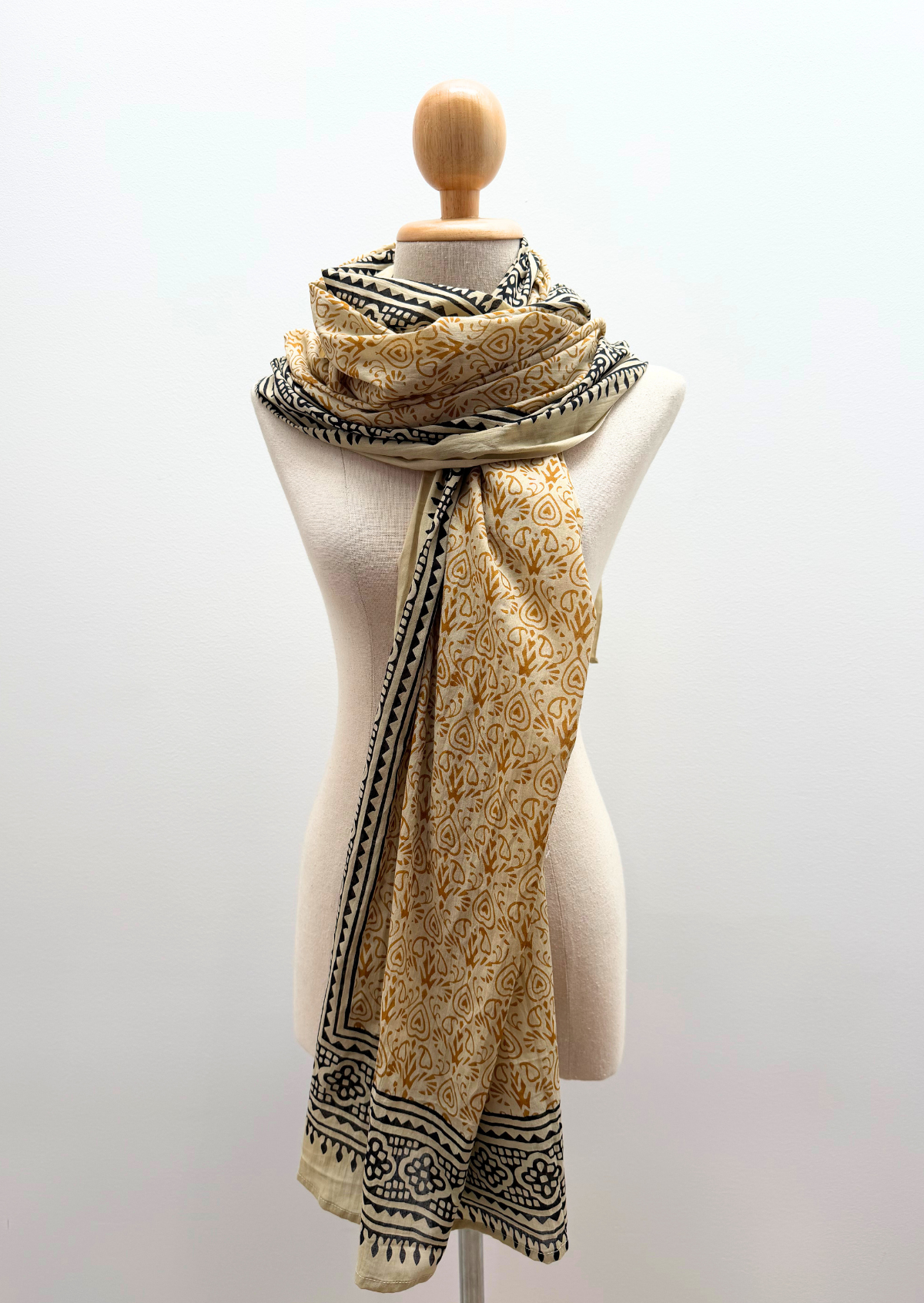 A lightweight patterned scarf draped on a cream-colored mannequin torso against a plain white background.