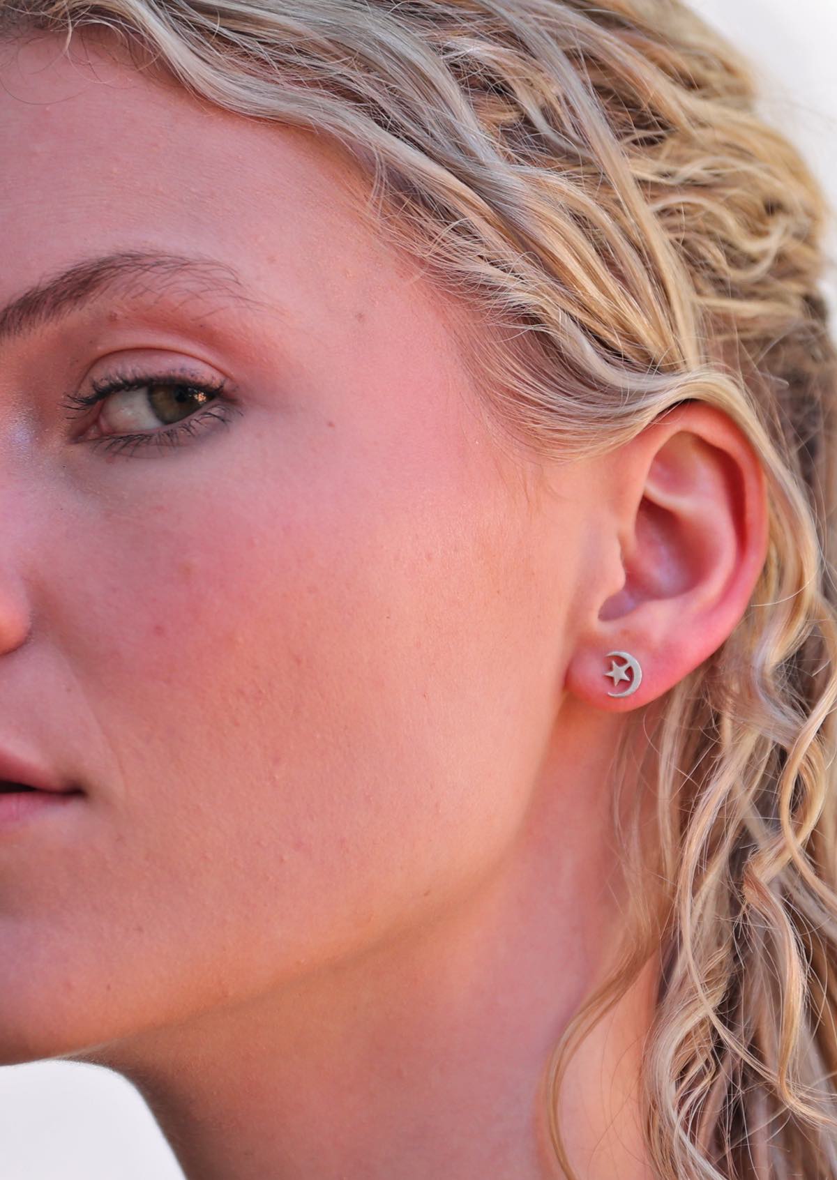 Woman wearing Moon and Stars silver stud earrings shaped like a crescent moon with a star inside it.