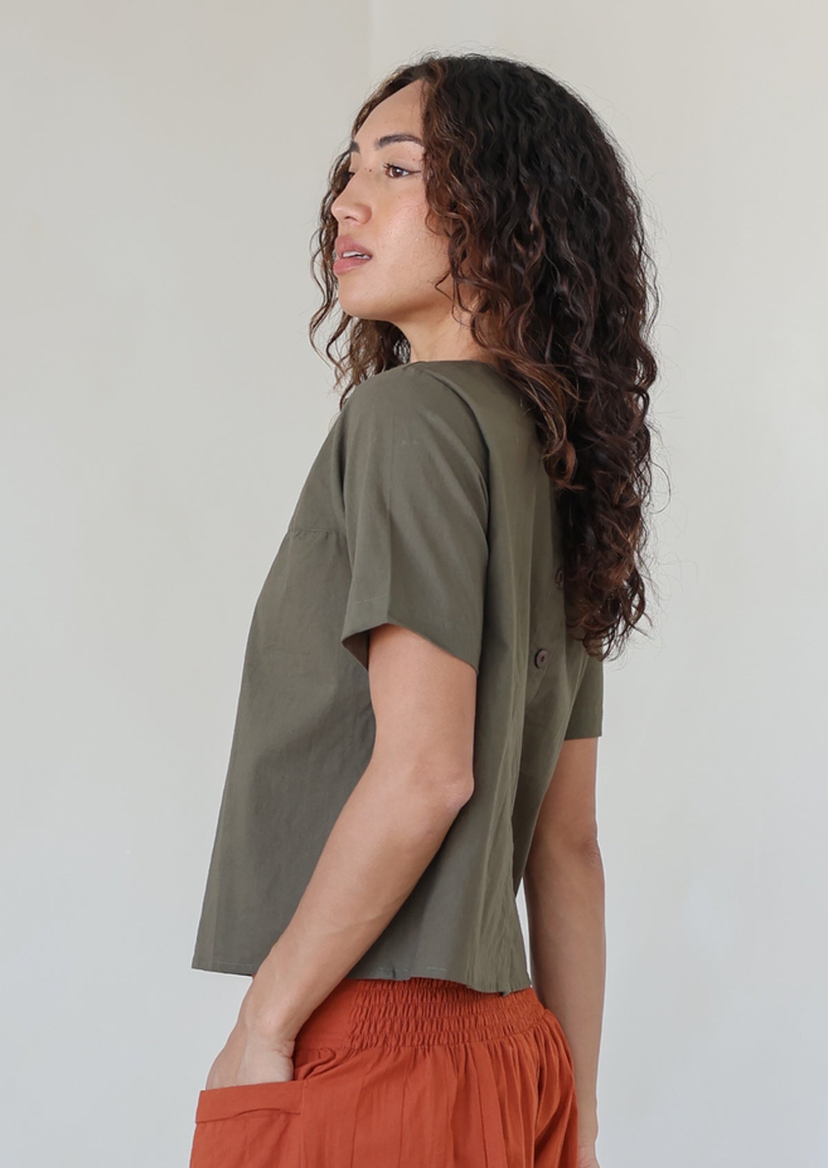 Model wearing a plain olive green shade top with non functional buttons down the back