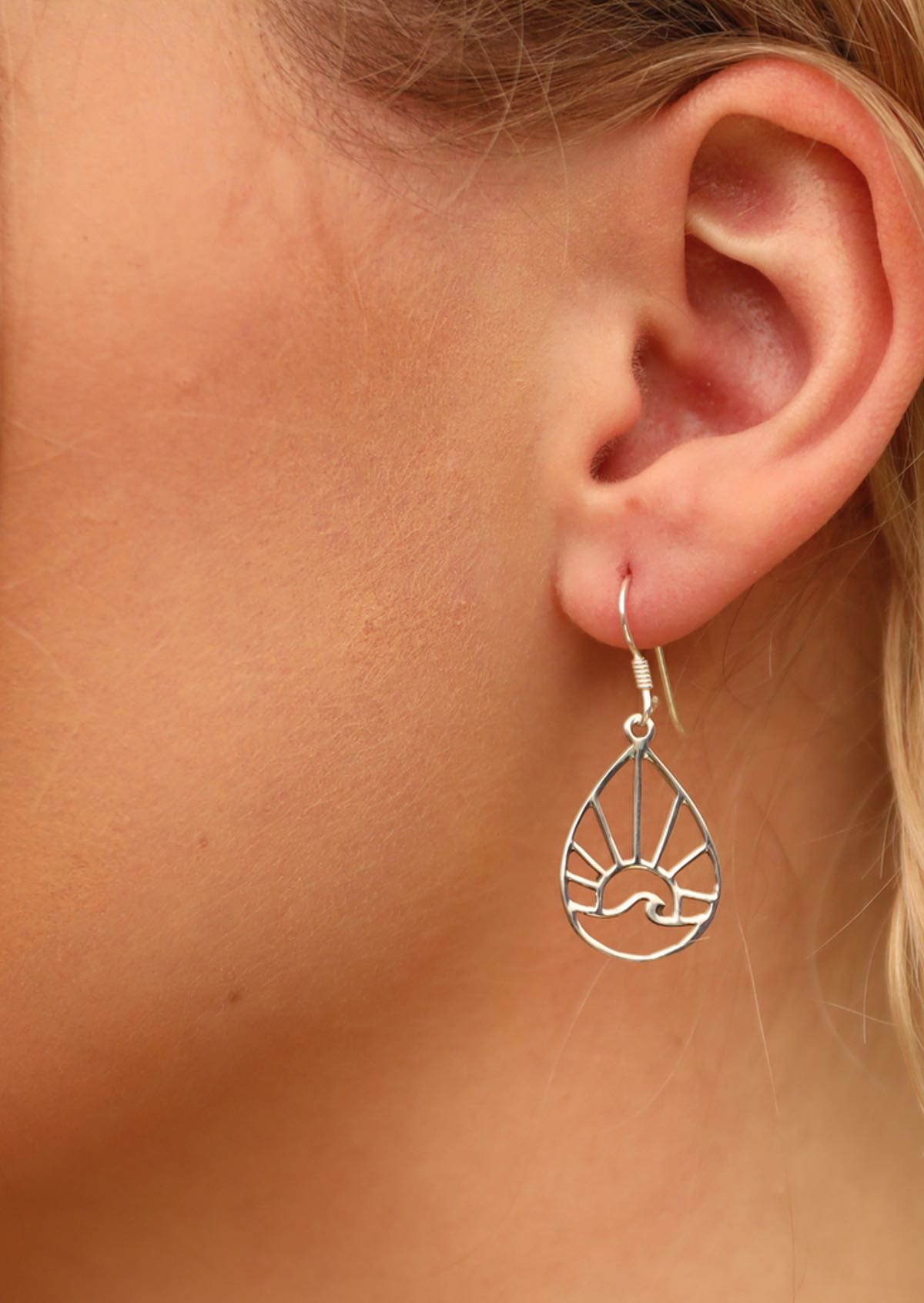 Model wearing silver earrings that are teardrop shape with a sun and wave within it