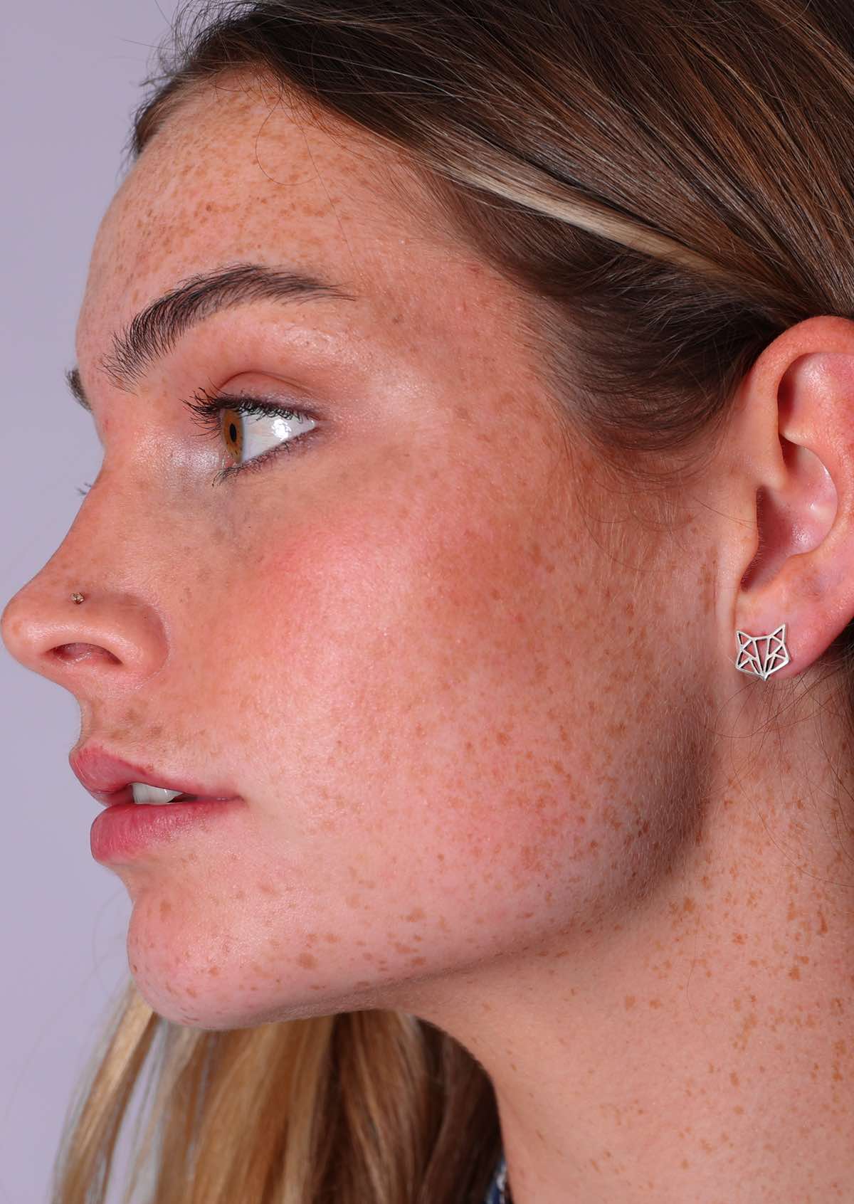 A close-up of a woman wearing sterling silver origami fox stud earrings.