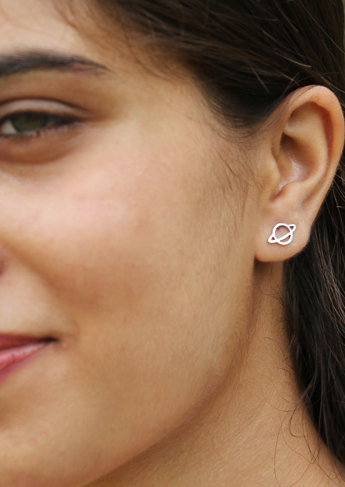 Close up of a woman wearing a silver saturn planet shaped studs with butterfly backs