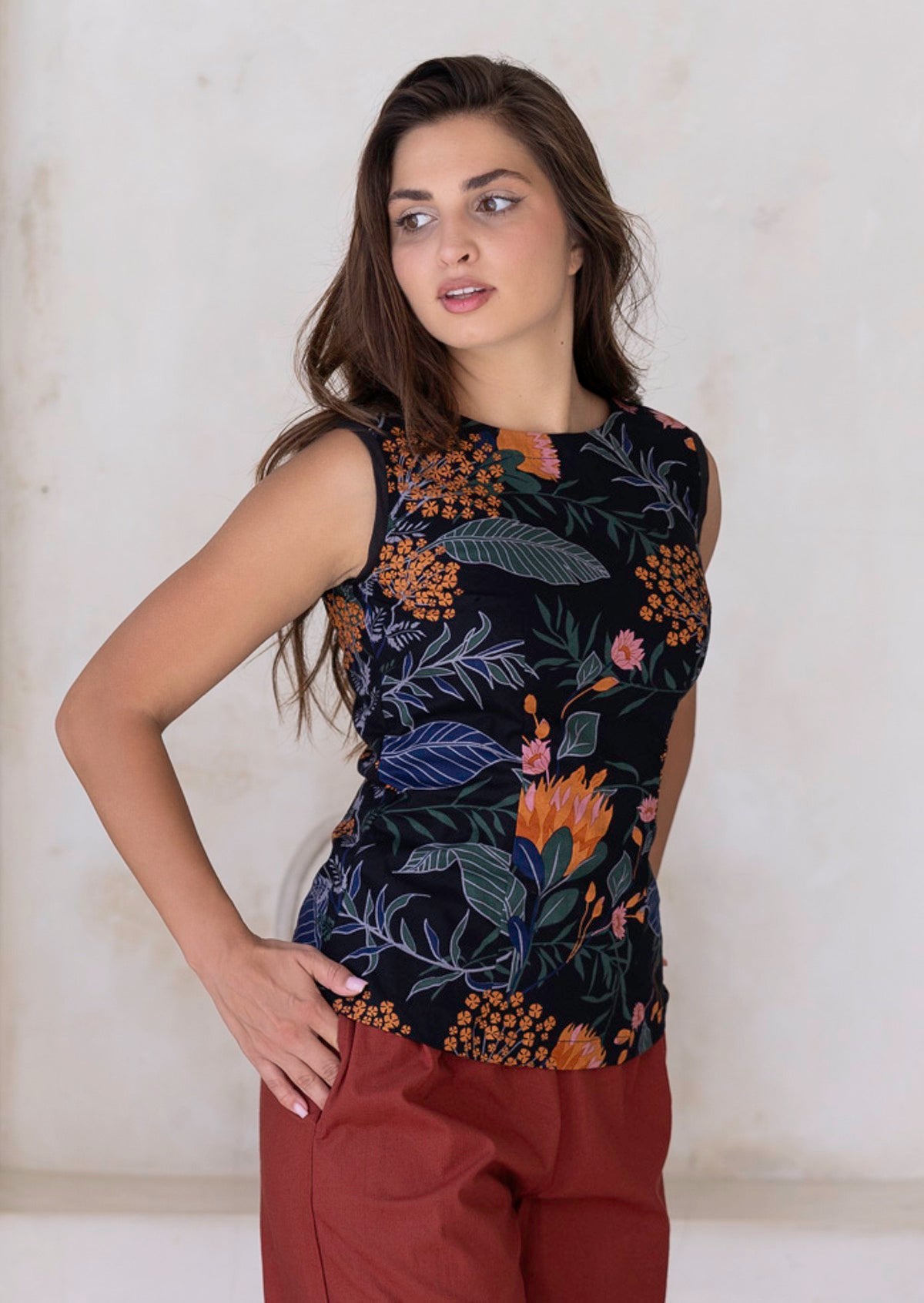 Woman poses with hand in pocket of pants, paired with a sleeveless cotton top with floral print
