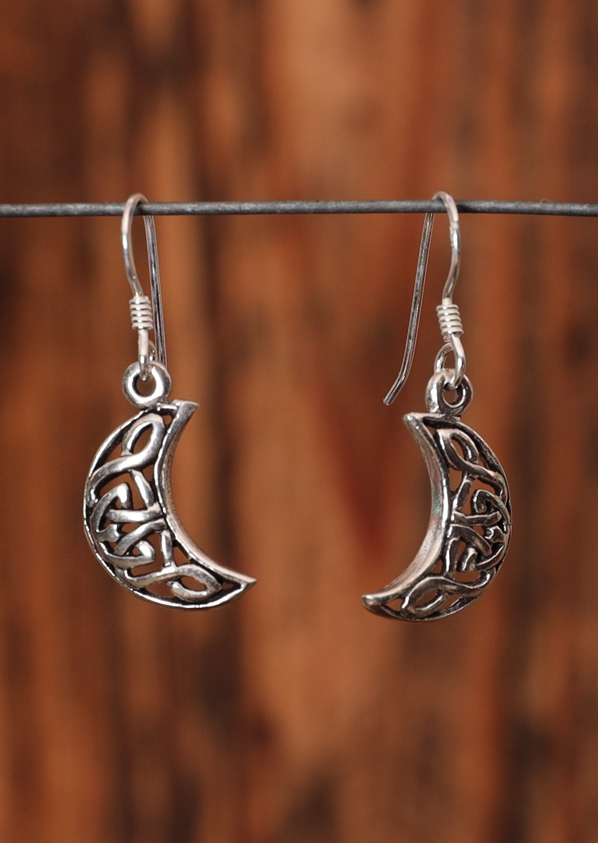 92.5% silver Celtic style hanging moon earrings sit on a wire for display.