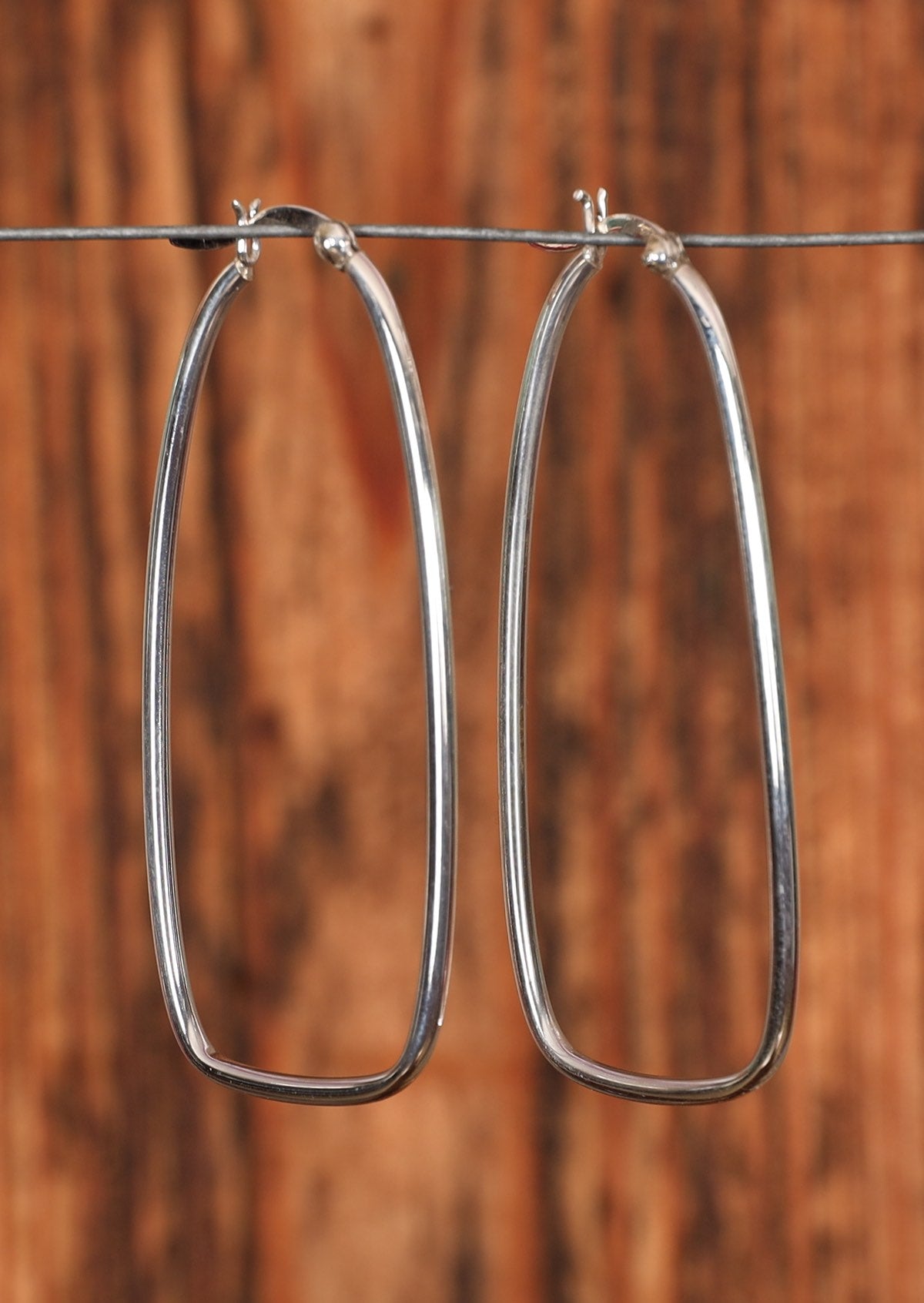 92.5% stretched silver hoop earrings sitting on a wire for display
