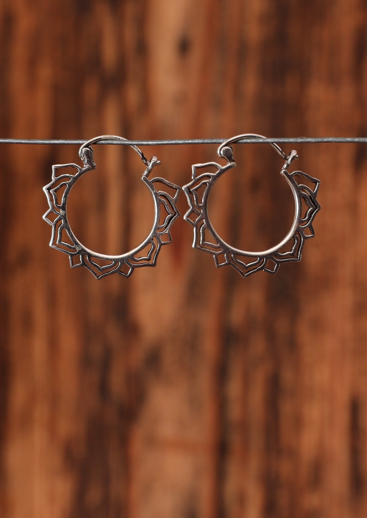 92.5% silver petal mandala earrings sit on a wire for display.