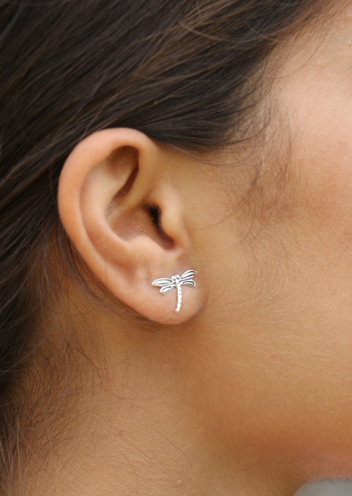 Close up of a person wearing dragonfly silver studs with intricate wing cutouts