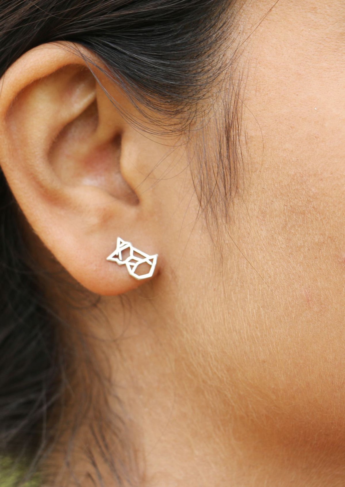 Close-up of an ear wearing a modern sterling silver fox studs with geometric design