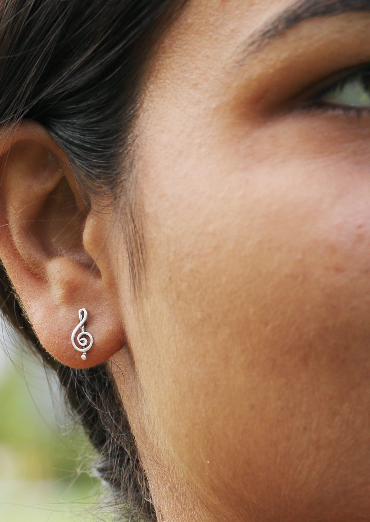 Woman wearing a delicate sterling silver treble clef studs with butterfly backs