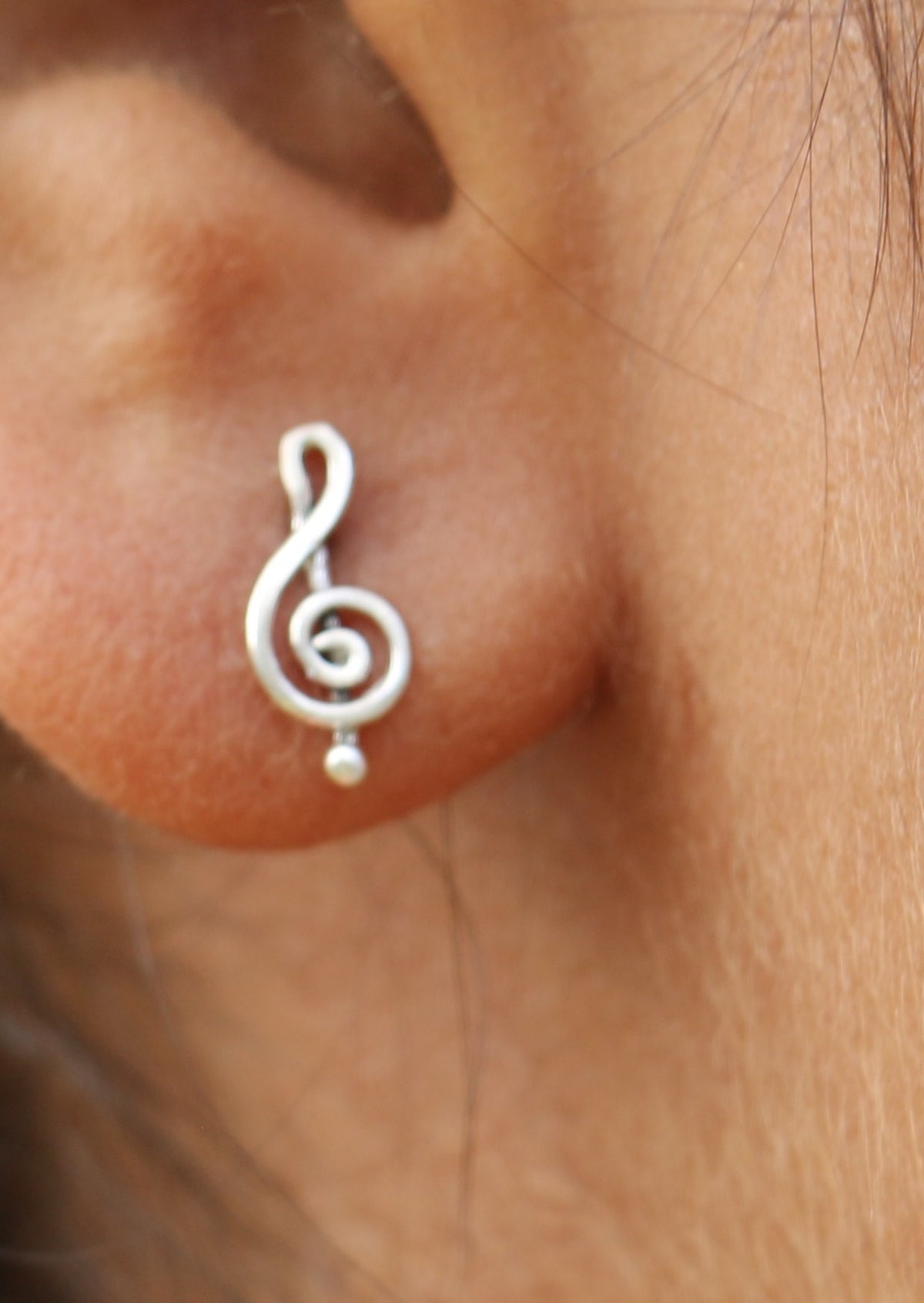 Silver treble clef minimalistic studs with a musical note design on a person's ear