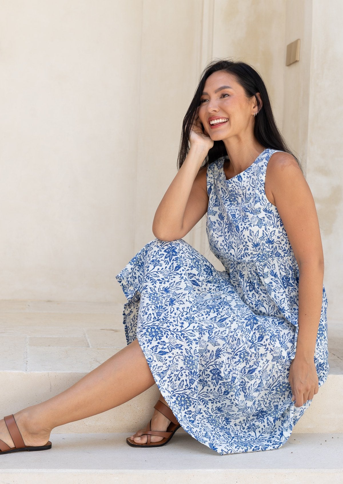 woman wearing a white based blue floral print cotton dress against a white background.