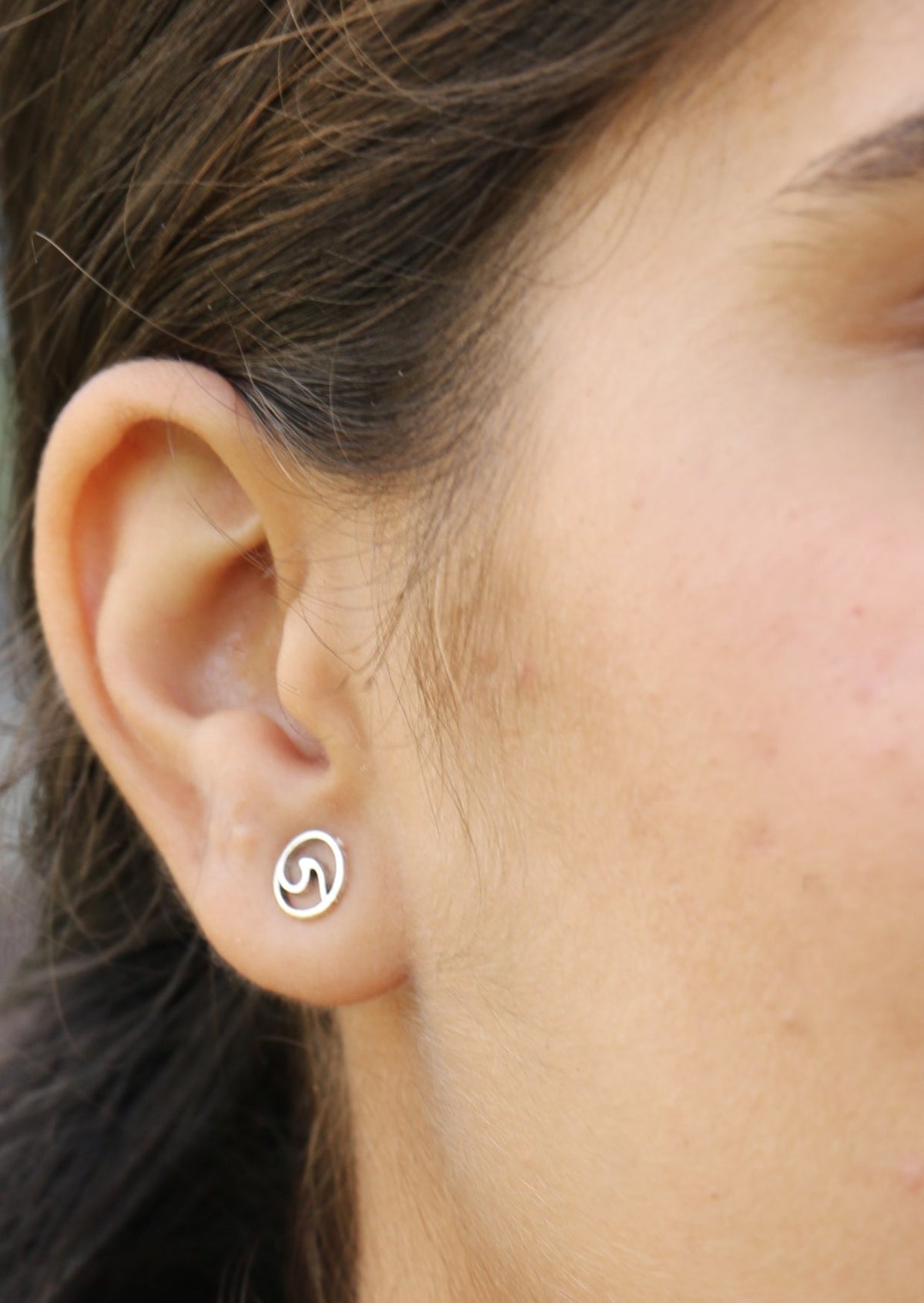 Close-up of an ear wearing a silver circular studs with cutout wave design
