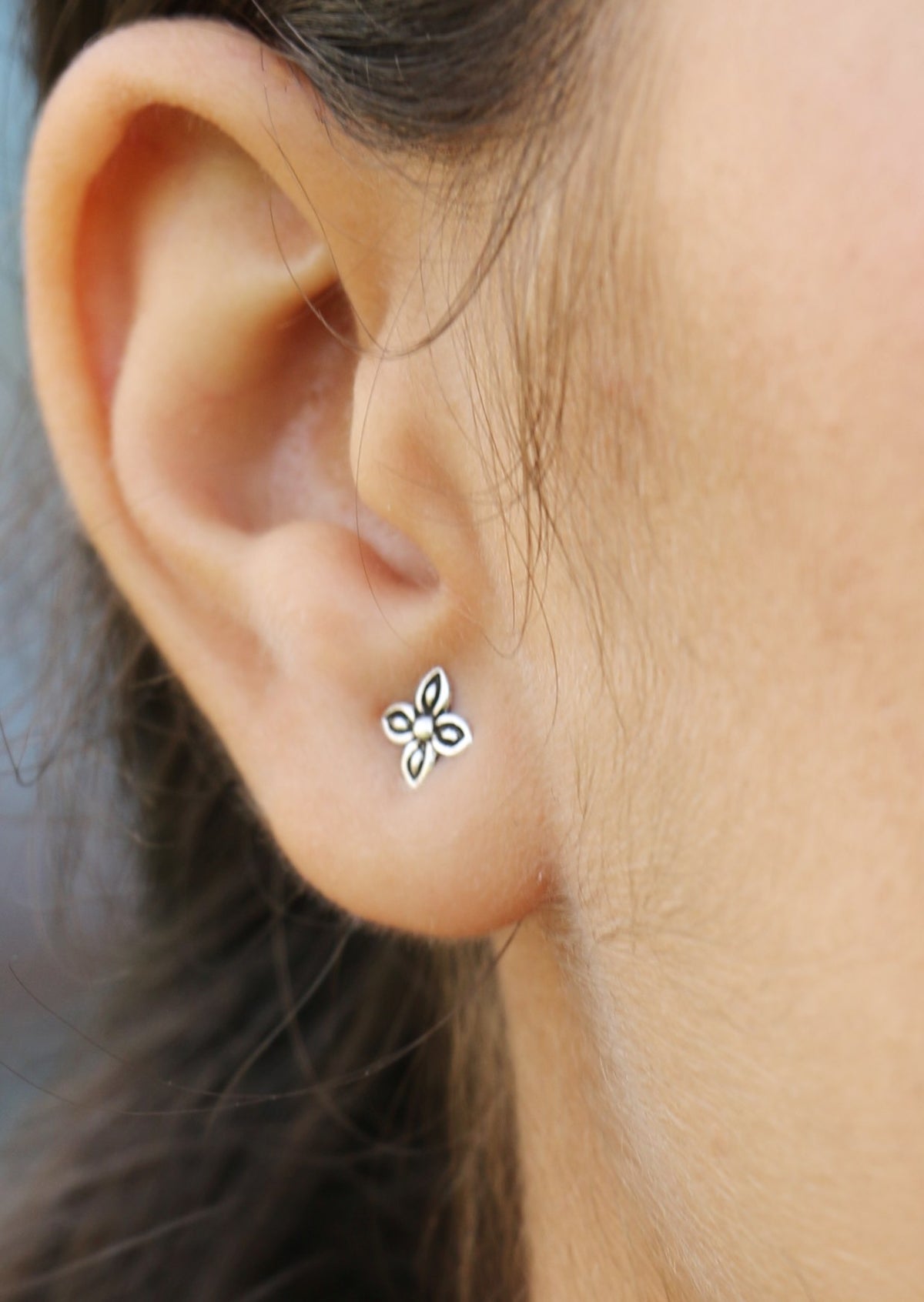 Close up of an ear wearing a silver floral stud with a four petal design