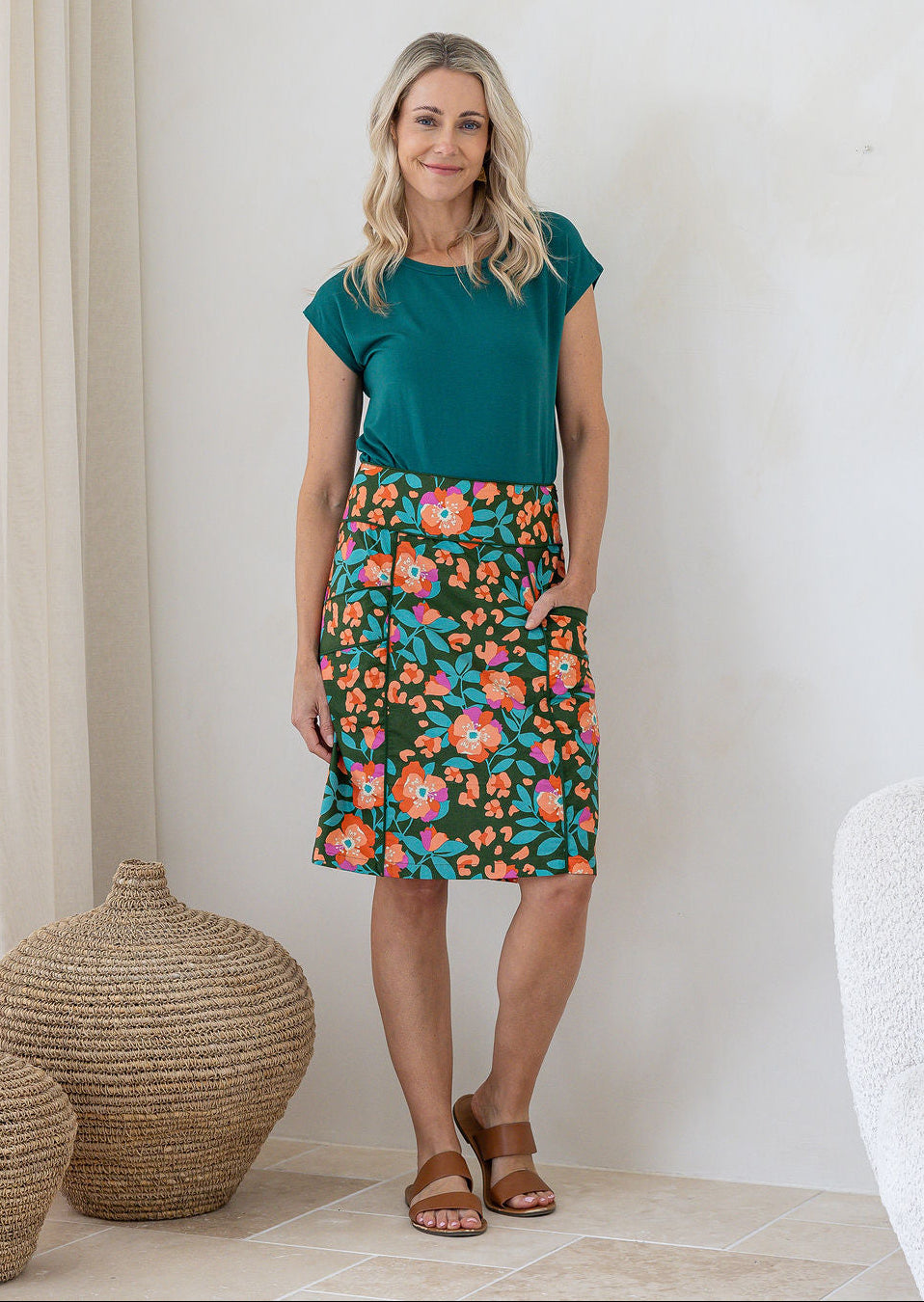 Woman stands in 100% cotton above knee length A-line skirt with piped detailing, pockets and a side zipper.