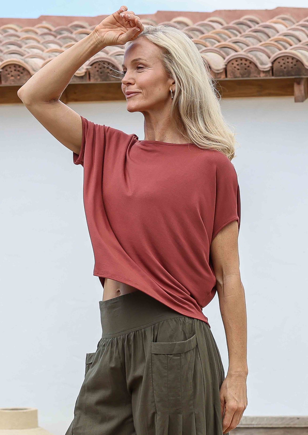 Woman with hand on forehead wearing 100% rayon batwing top in terracotta standing in front of a white house