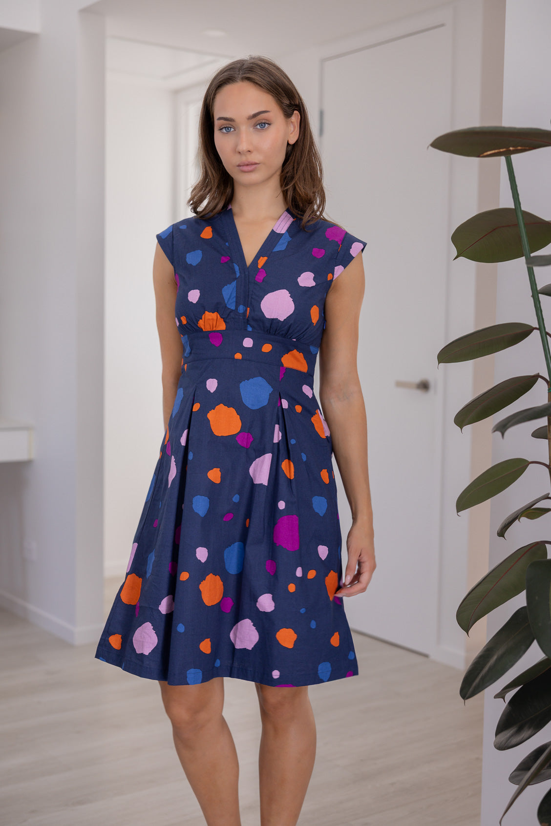 Woman wears 100% Cotton Bold Spotty Print Dress with tailored v-neckline, empire waistline, a-line skirt and side zipper