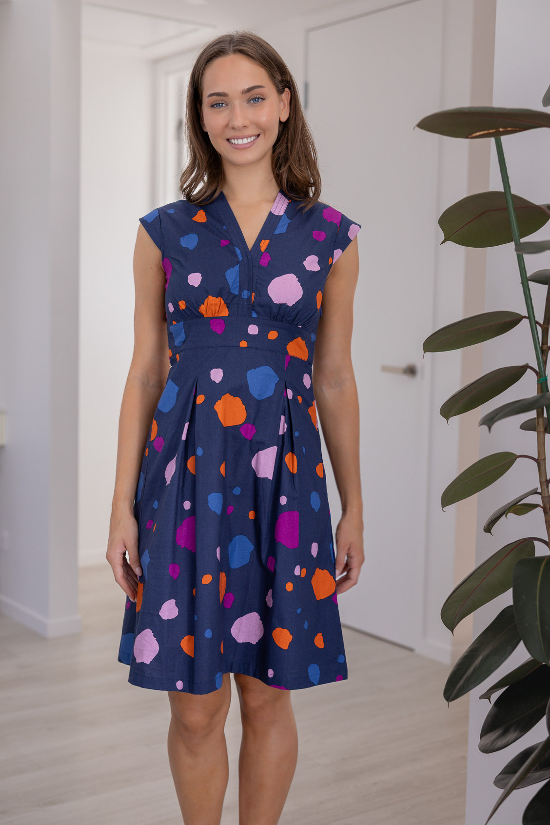 Woman wears 100% cotton bold spotty print dress with tailored v-neckline, empire waistline, a-line skirt and side zipper