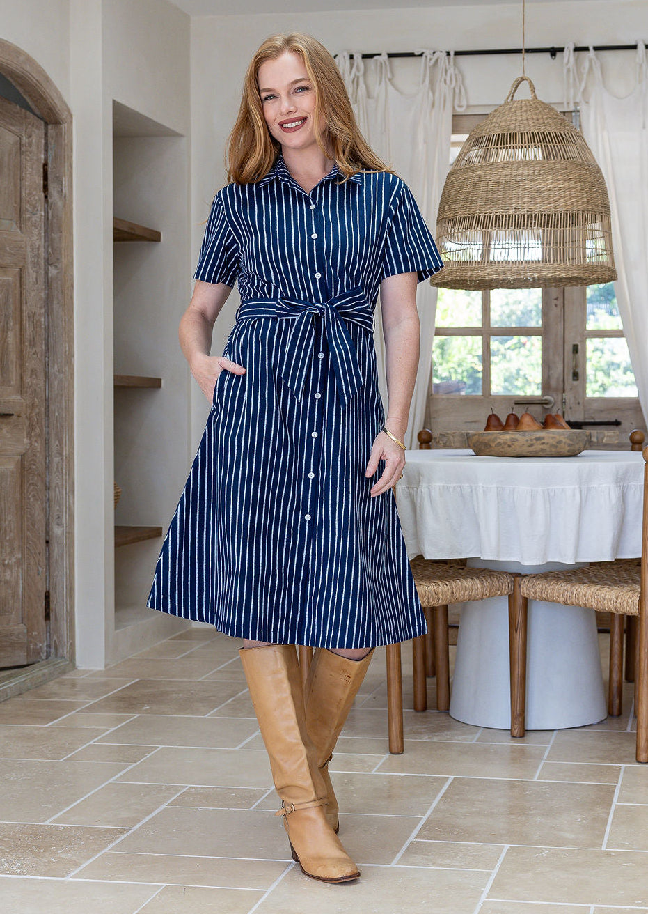 Woman wearing 100 percent cotton button through shirt dress with collar and short sleeves, in a navy based white striped print.