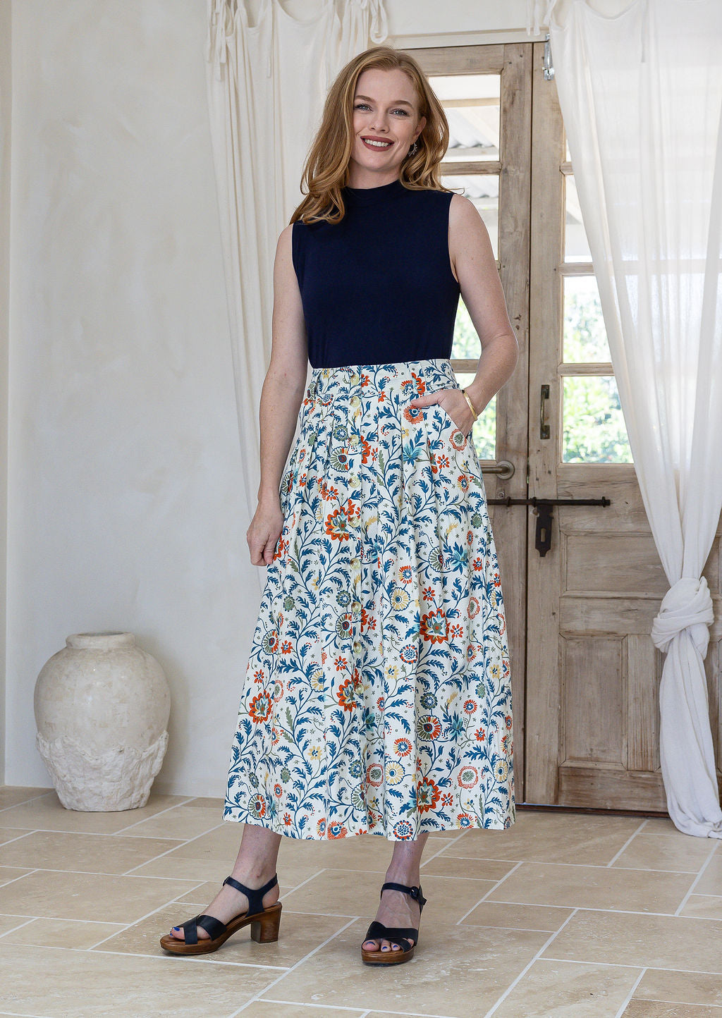 Woman standing with one hand in pocket wears 100% cotton button through skirt in white based floral print.