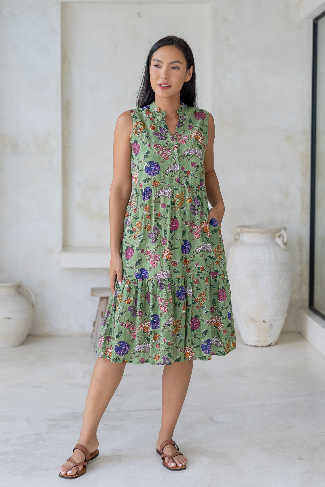 Woman wearing a sleeveless green floral cotton dress with pockets, mandarin collar and a two tiered skirt.