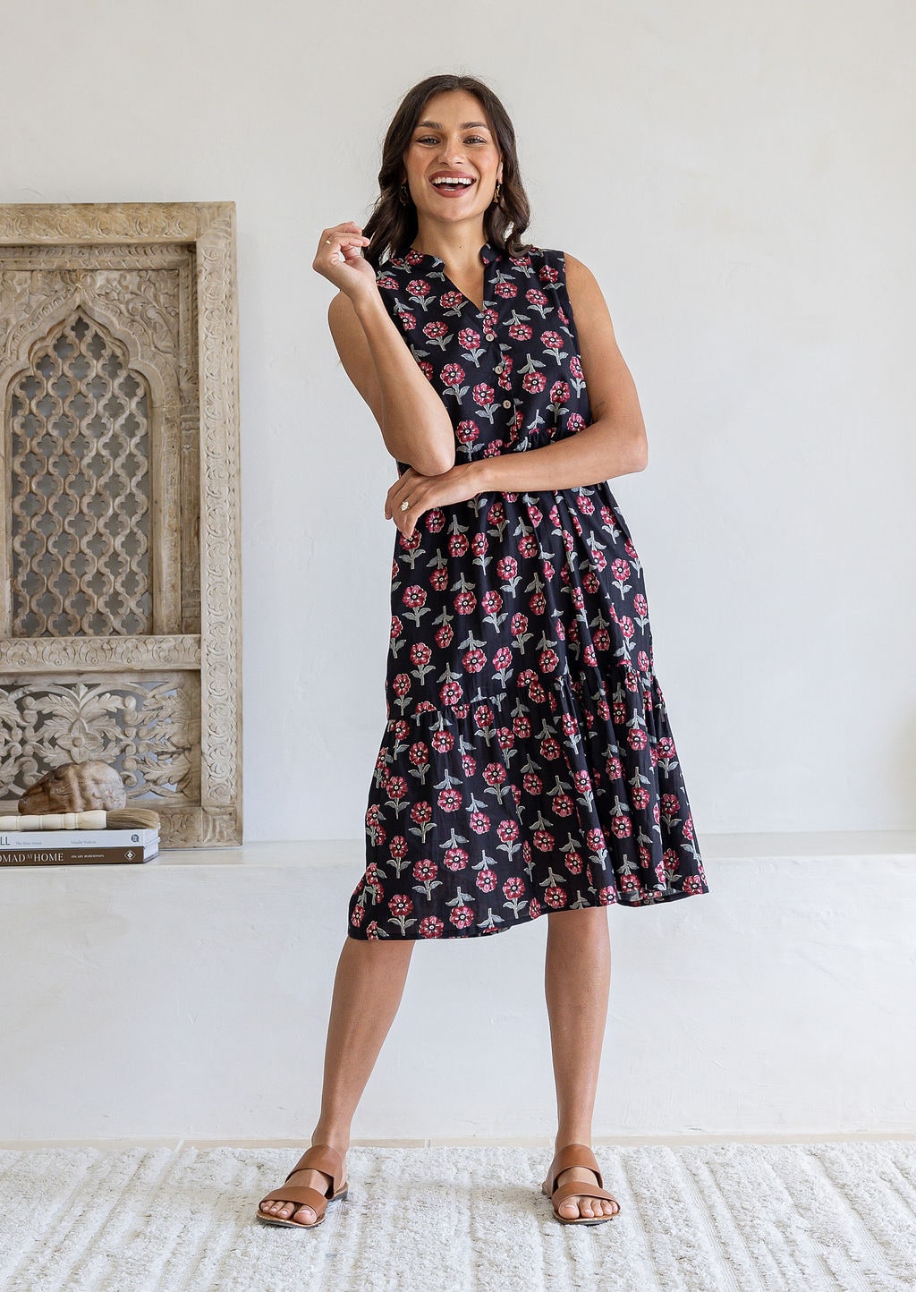 A woman modelling a sleeveless black based floral print cotton midi dress with a one hand in pockets