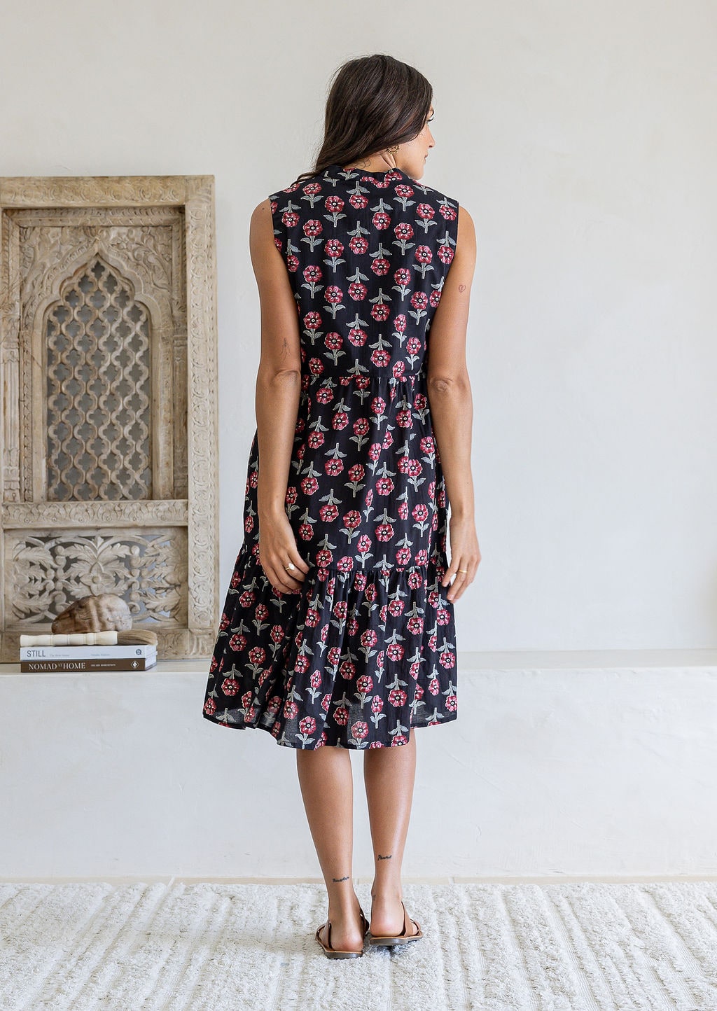 Woman stands backwards wearing a sleeveless navy floral cotton dress with pockets, mandarin collar and a two tiered skirt.