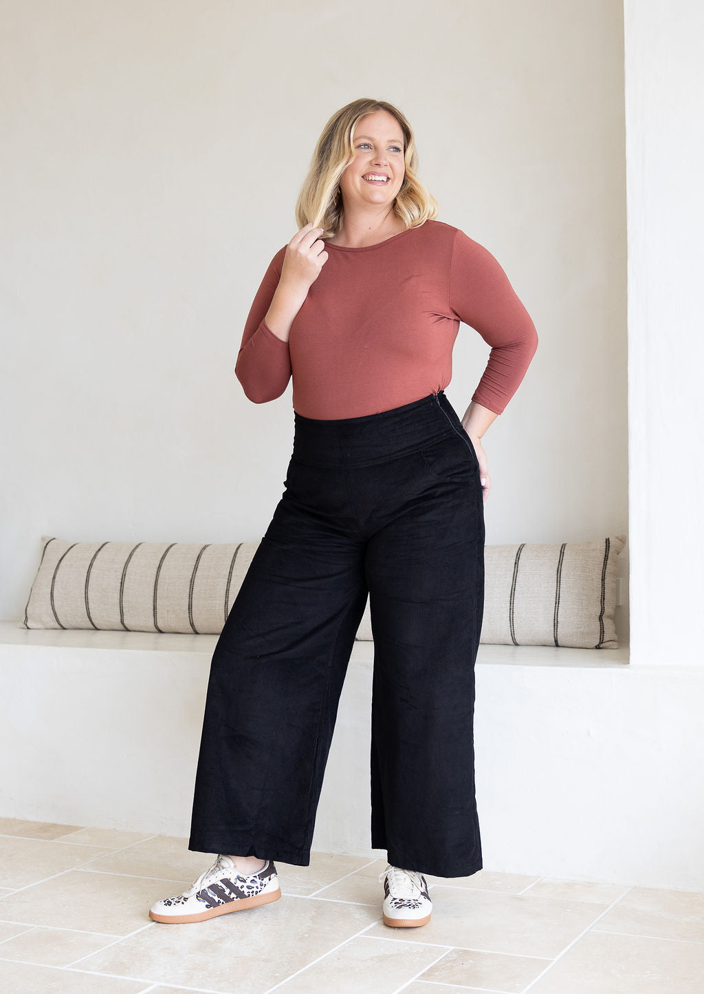 Woman wearing black corduroy wide legged pants with long sleeve boat neck pink top