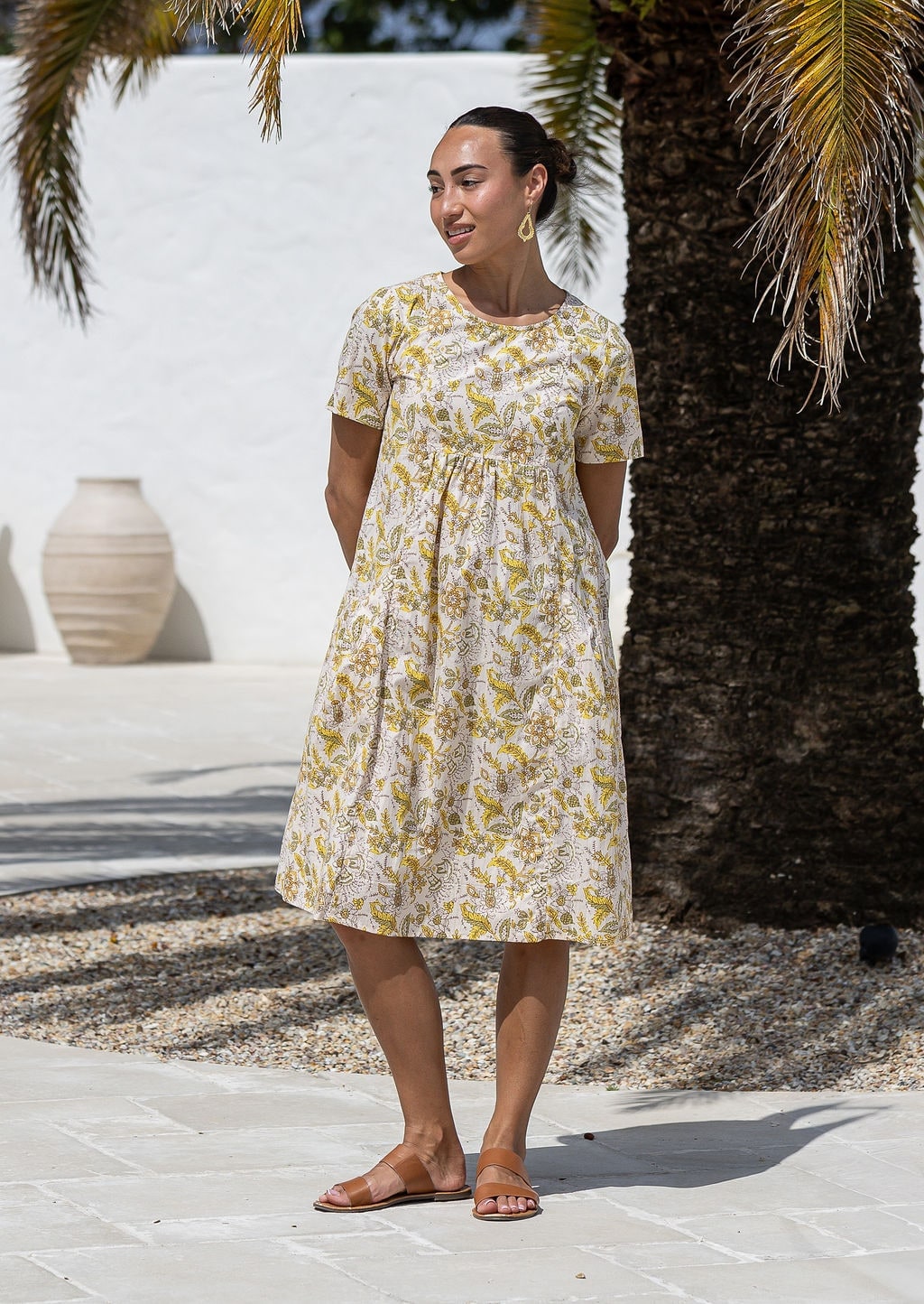 Woman poses in a cream based cotton floral short sleeve dress with round neckline