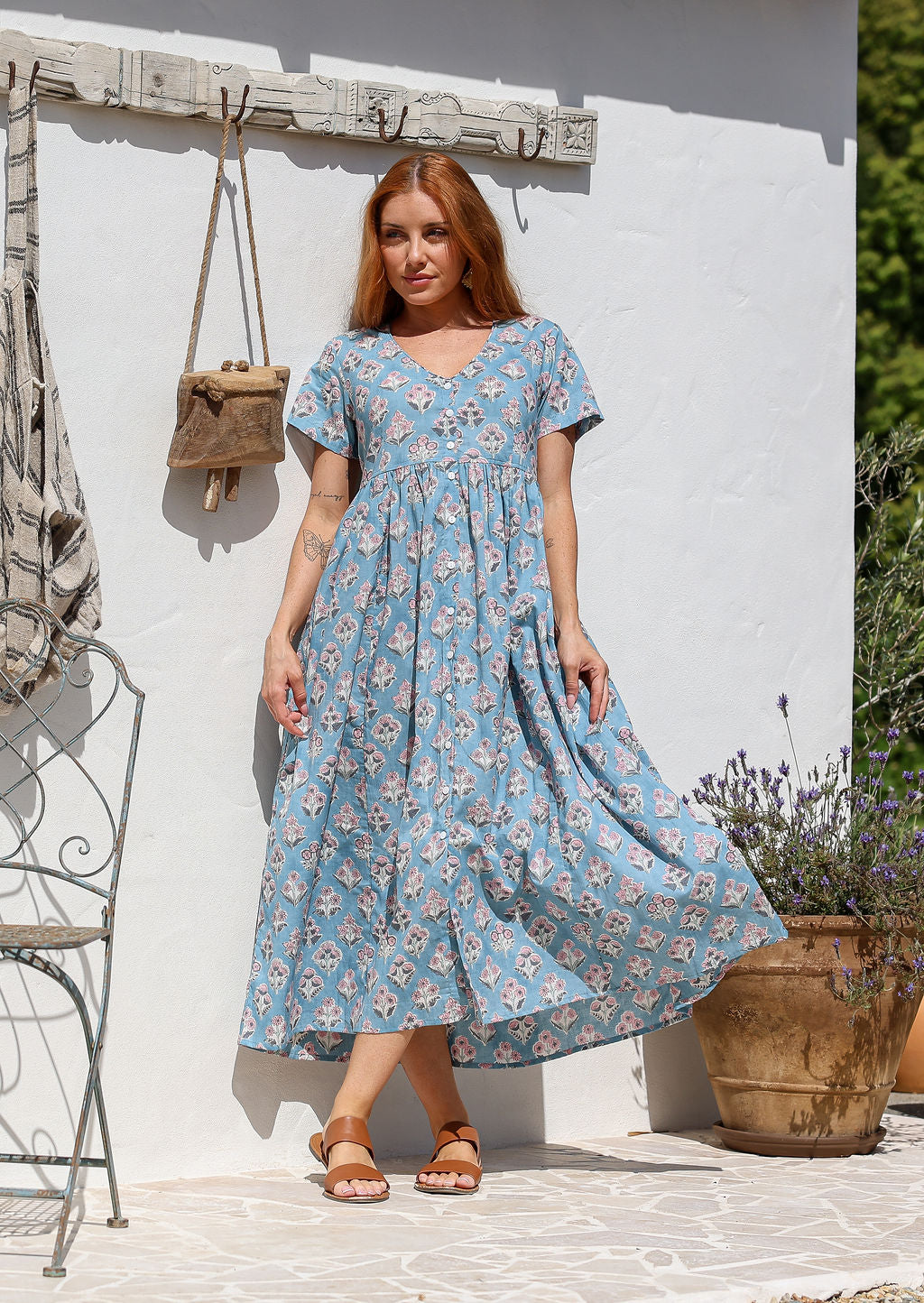 A woman wearing a powder blue cotton midi dress with short sleeves, a V-neckline, and is button-through.