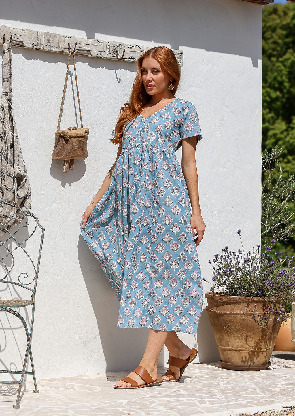 Woman stands sideways wearing a 100% cotton dress with short sleeves, pockets, and a drawstring tie at the back.