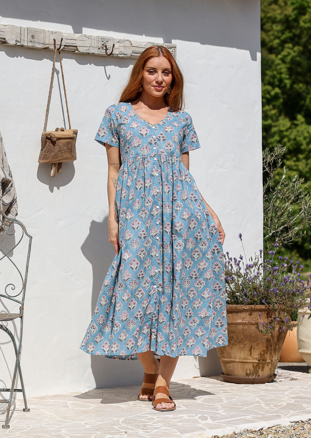 Woman standing in a 100% cotton floral print dress with a V-neckline, short sleeves, pockets, and buttons through to the knee.