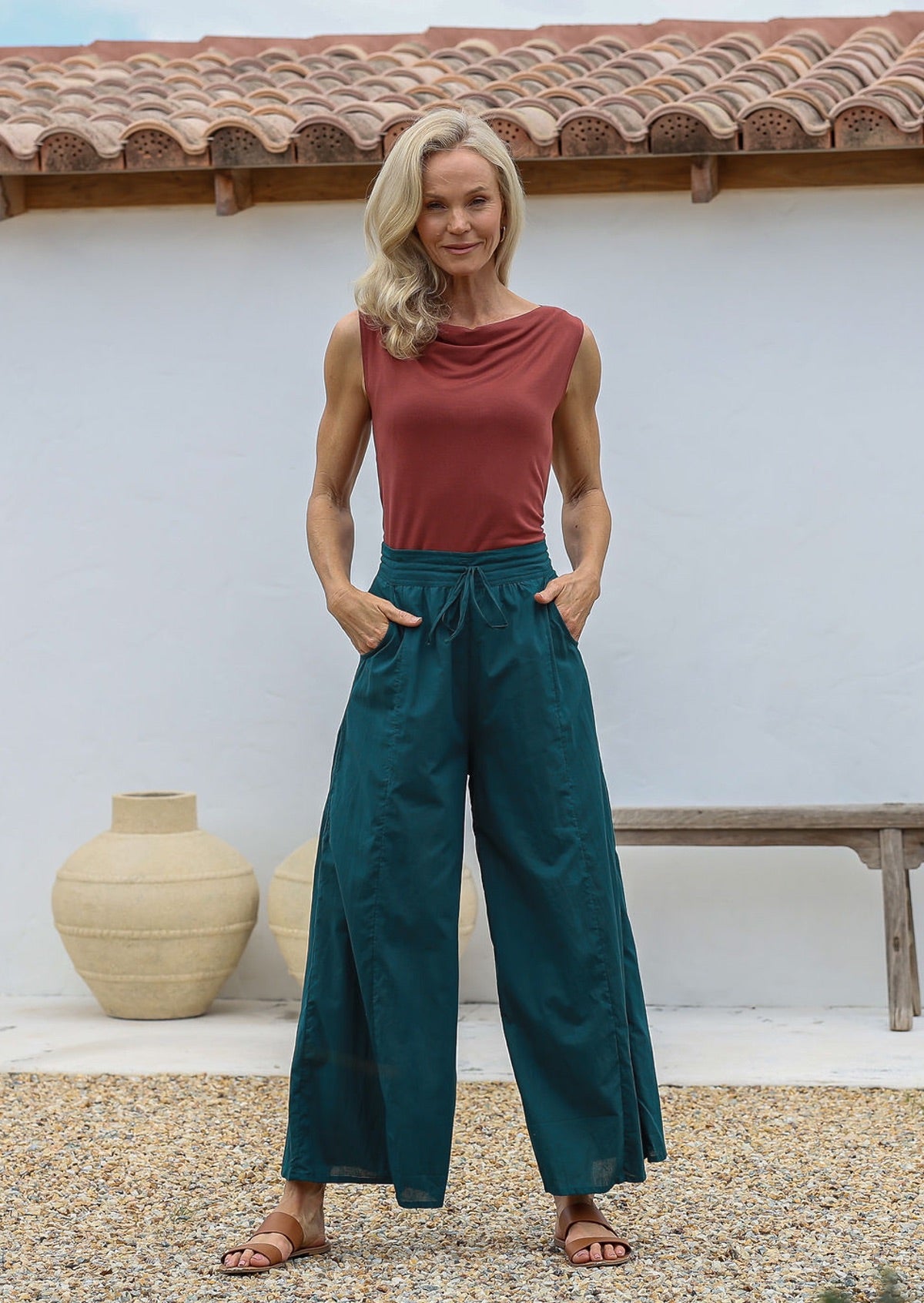 Woman wearing a cowl neck top and deep teal wide-leg pants with pockets, drawstring and elasticated waist.